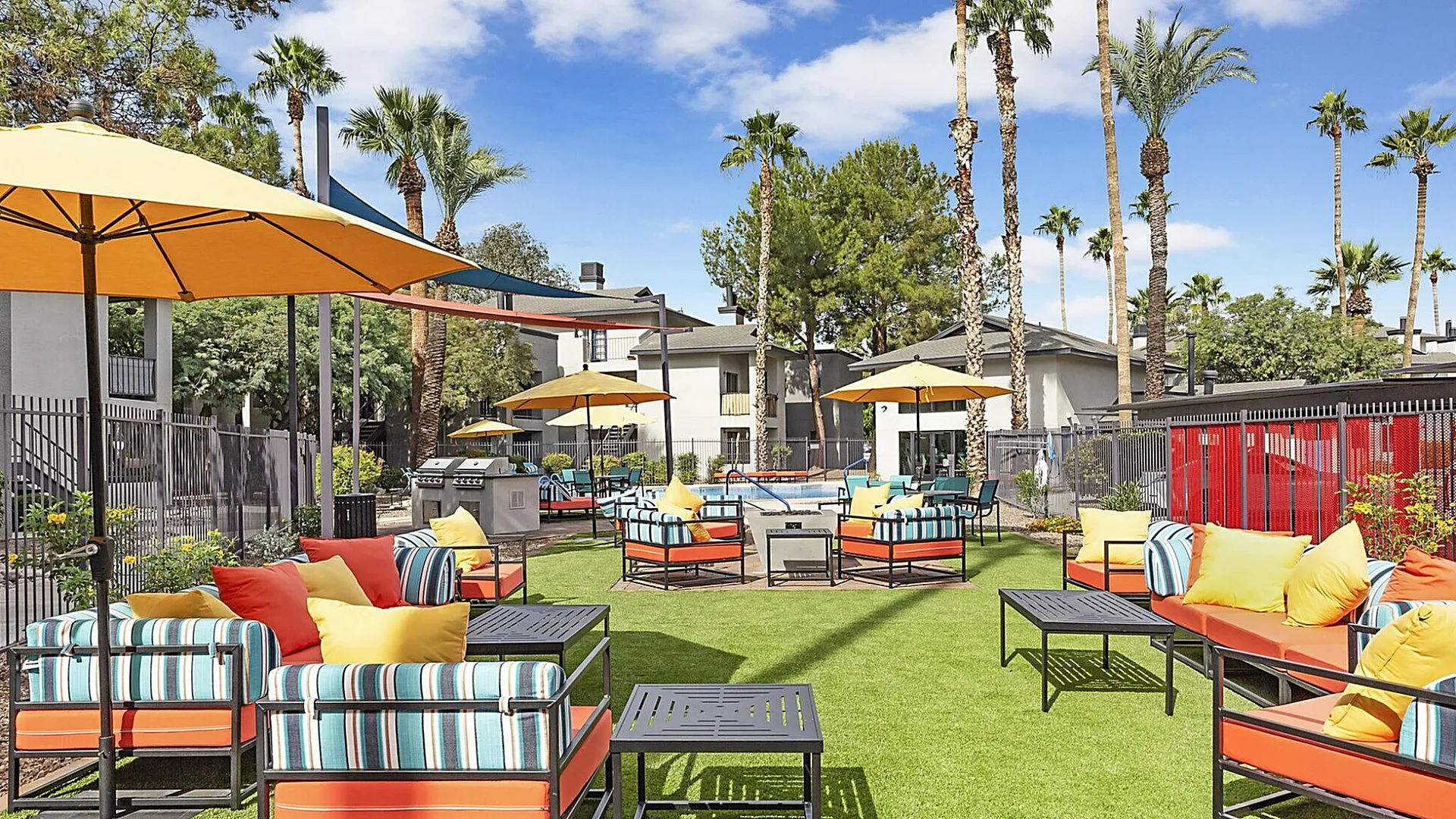 Vibrant outdoor lounge area with colorful seating, perfect for relaxation under the sun, surrounded by lush palm trees and bright umbrellas.