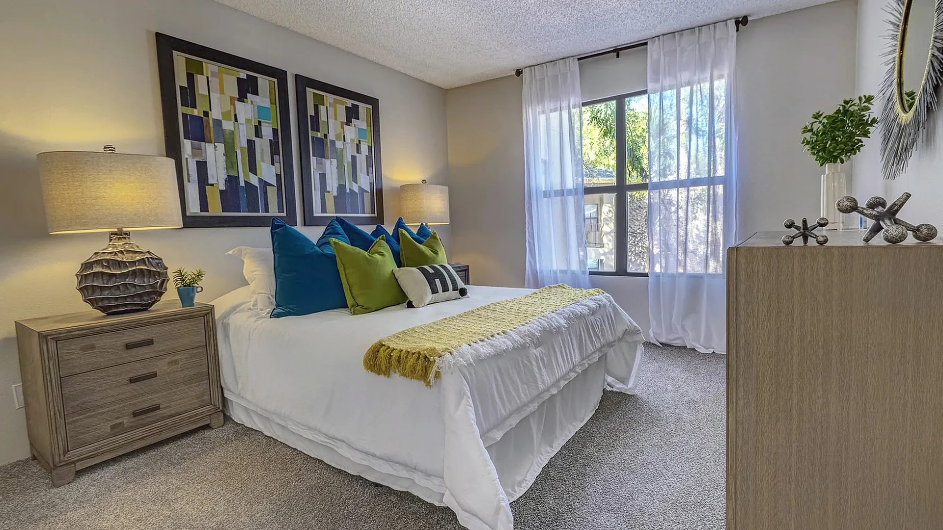 Chic bedroom with vibrant decor, featuring cozy bedding, stylish artwork, and abundant natural light through large windows.