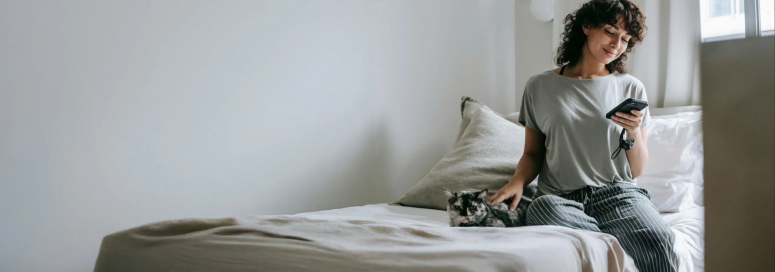 Cozy bedroom scene with a woman relaxing on a bed while using her smartphone, creating an inviting and serene ambiance.