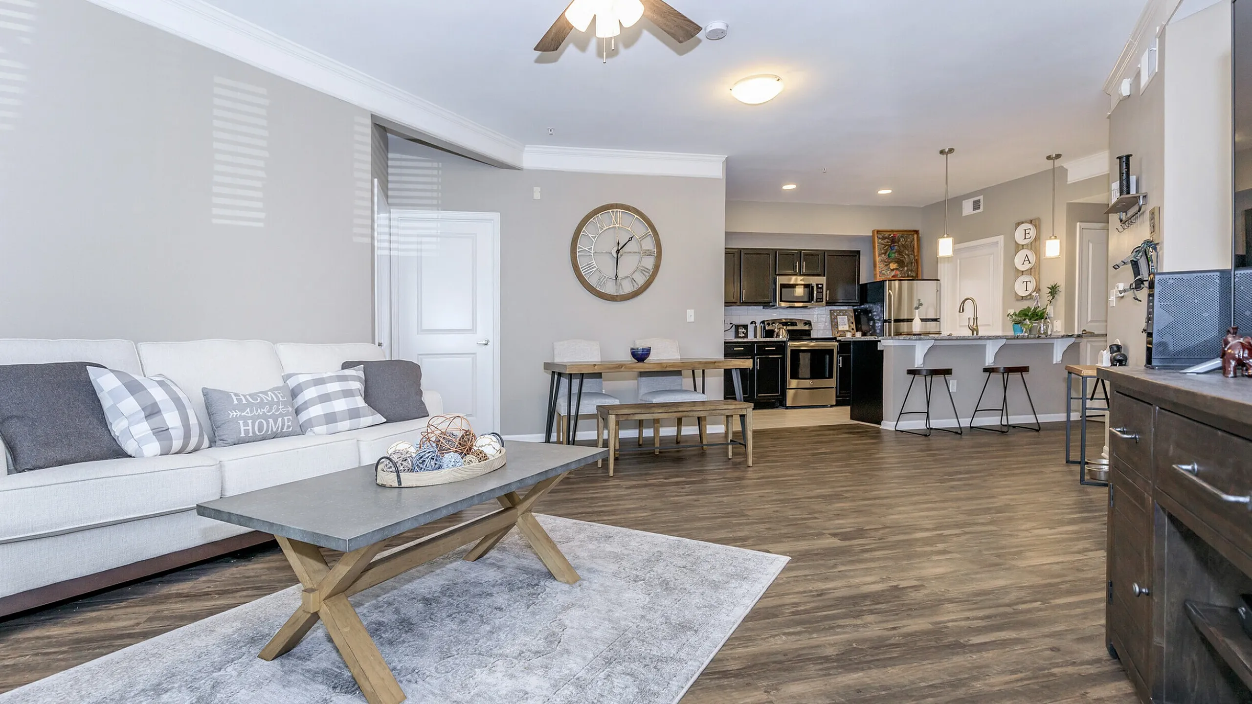 Corbin Crossing open-concept living room with sleek kitchen, wood flooring, and cozy beige sofa, perfect for urban living.