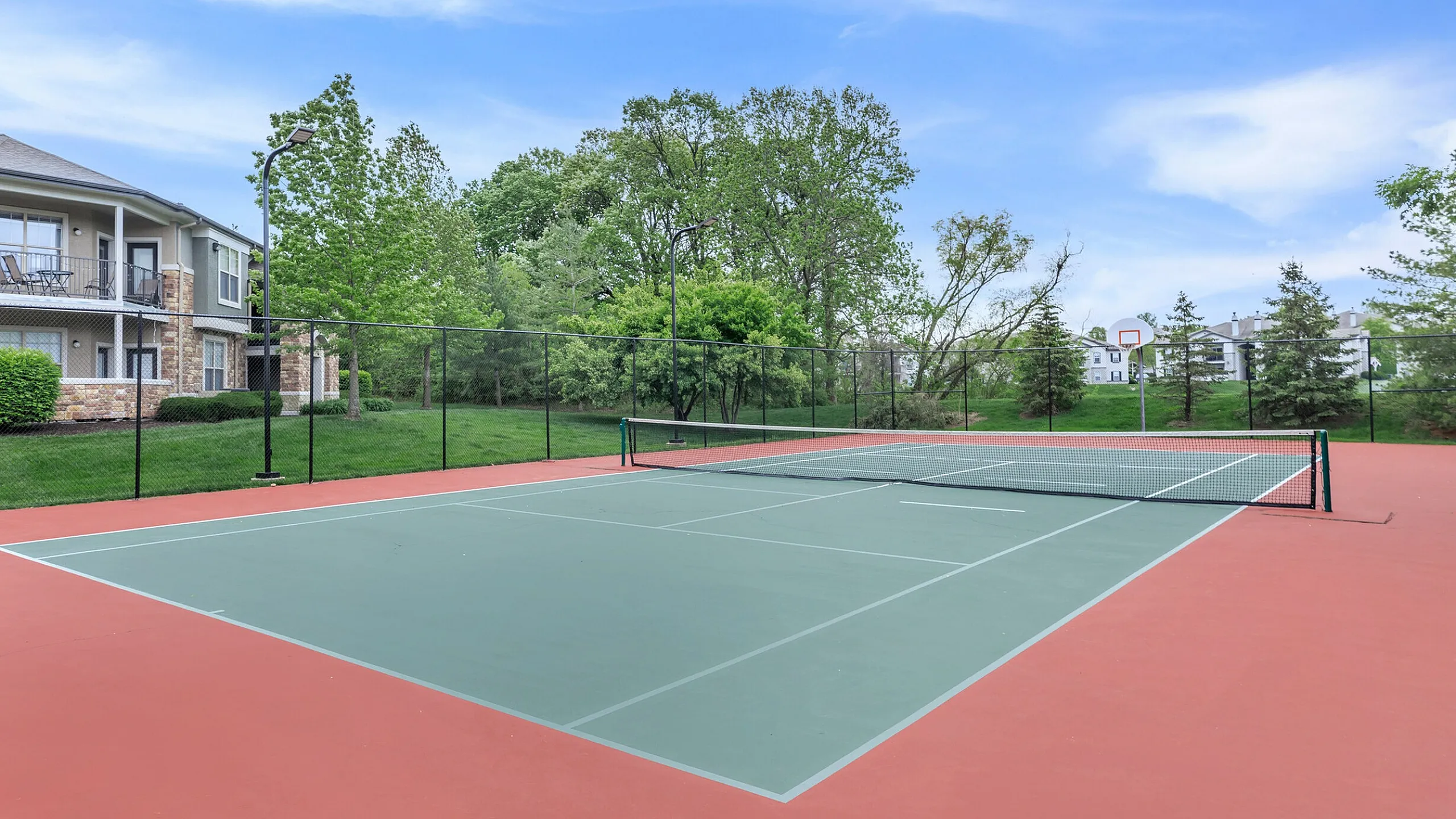 Corbin Crossing outdoor tennis court nestled in a lush apartment community, offering leisure and recreation in a beautiful green setting.