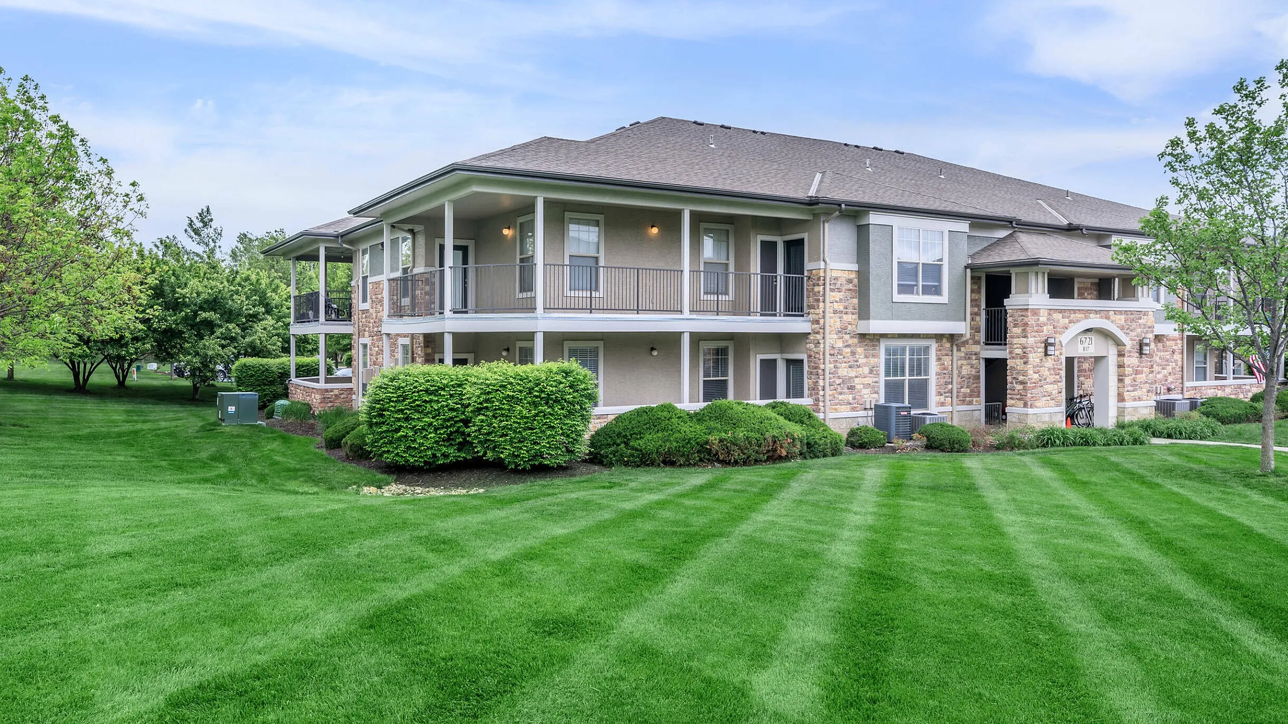 Corbin Crossing apartment complex with elegant stone facade, surrounded by lush green lawns and mature trees, offering a serene living environment.