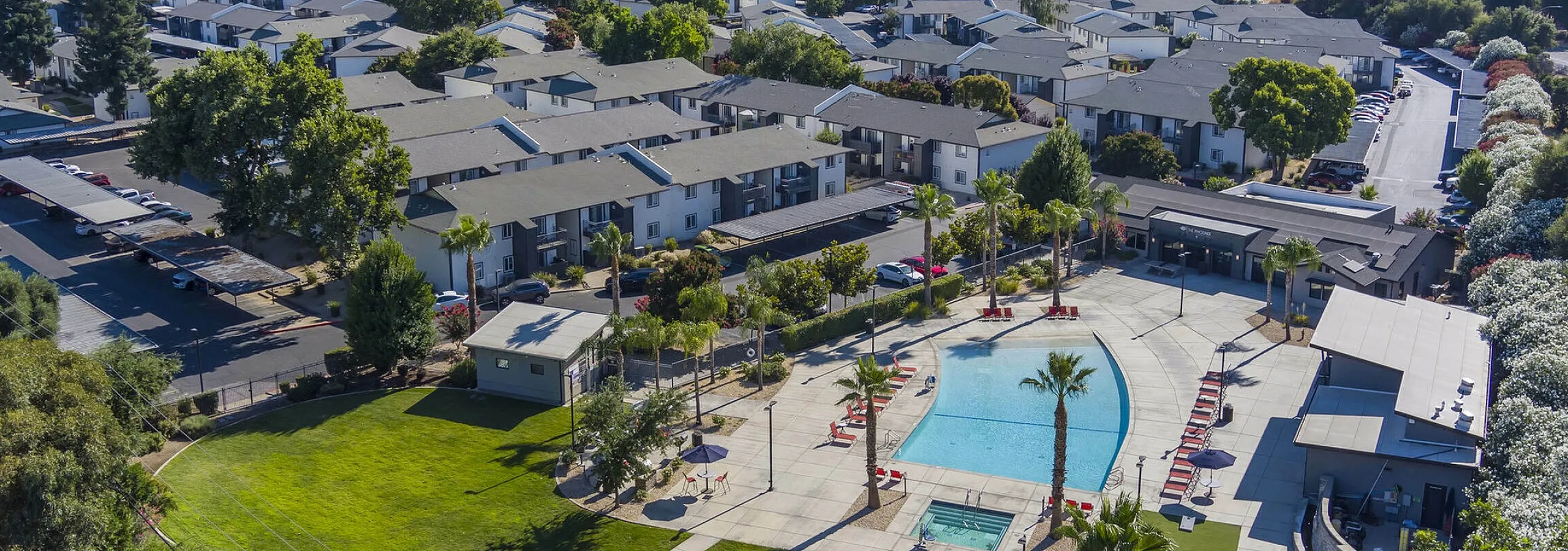 Aerial view of a The Phoenix Sacramento apartment complex with beautifully landscaped gardens, a large swimming pool, and spacious outdoor recreation area, surrounded by lush greenery.