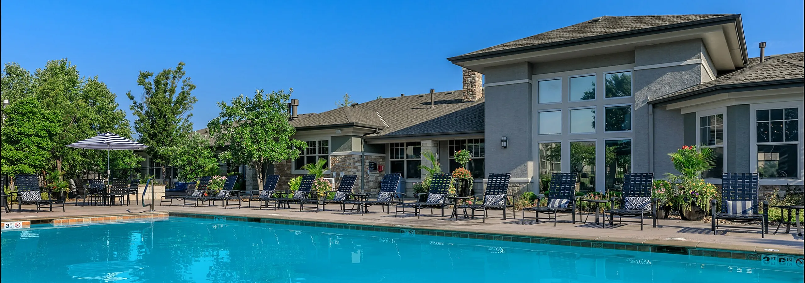 Corbin Crossing outdoor pool area with lounge chairs and beautiful landscaping, perfect for relaxation and leisure in a modern apartment community.