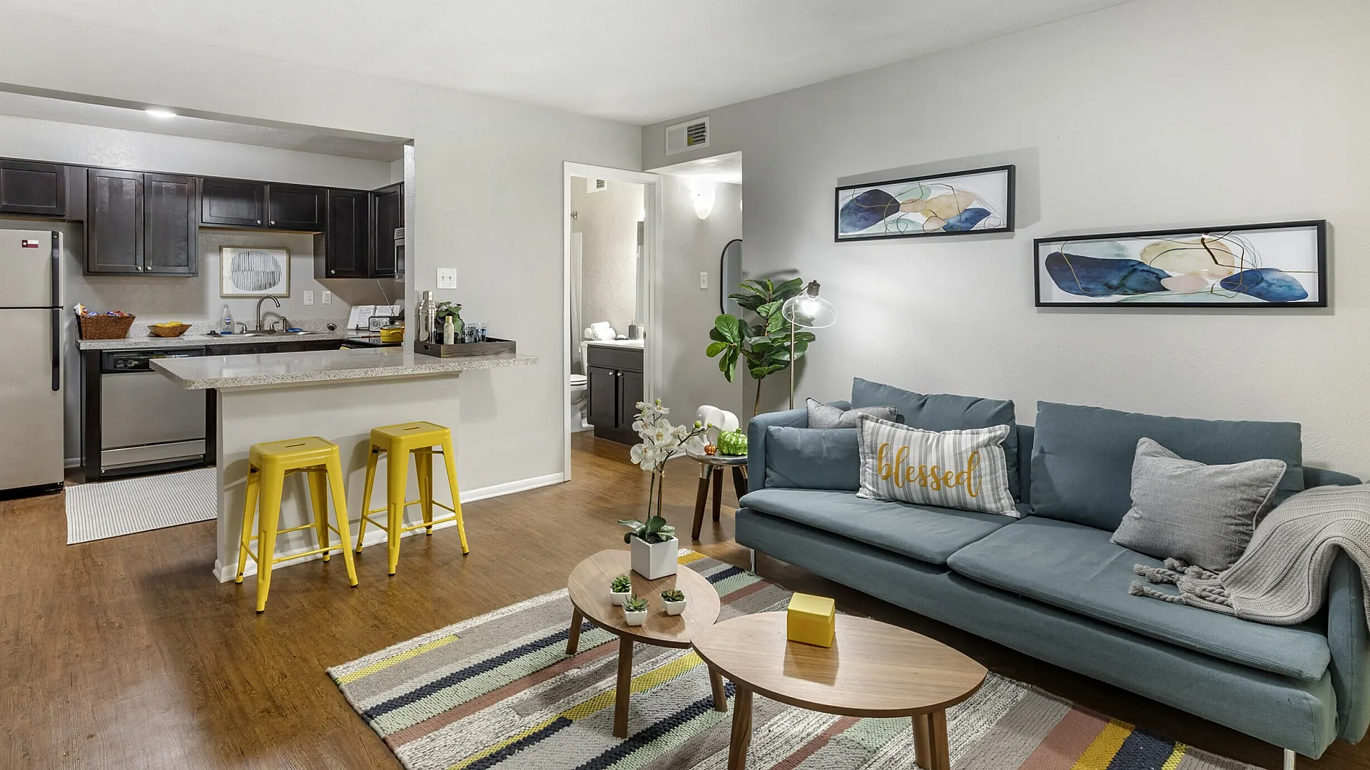 Modern open-concept living room and kitchen with yellow bar stools at The Venue student apartments in Denton, TX near University of North Texas
