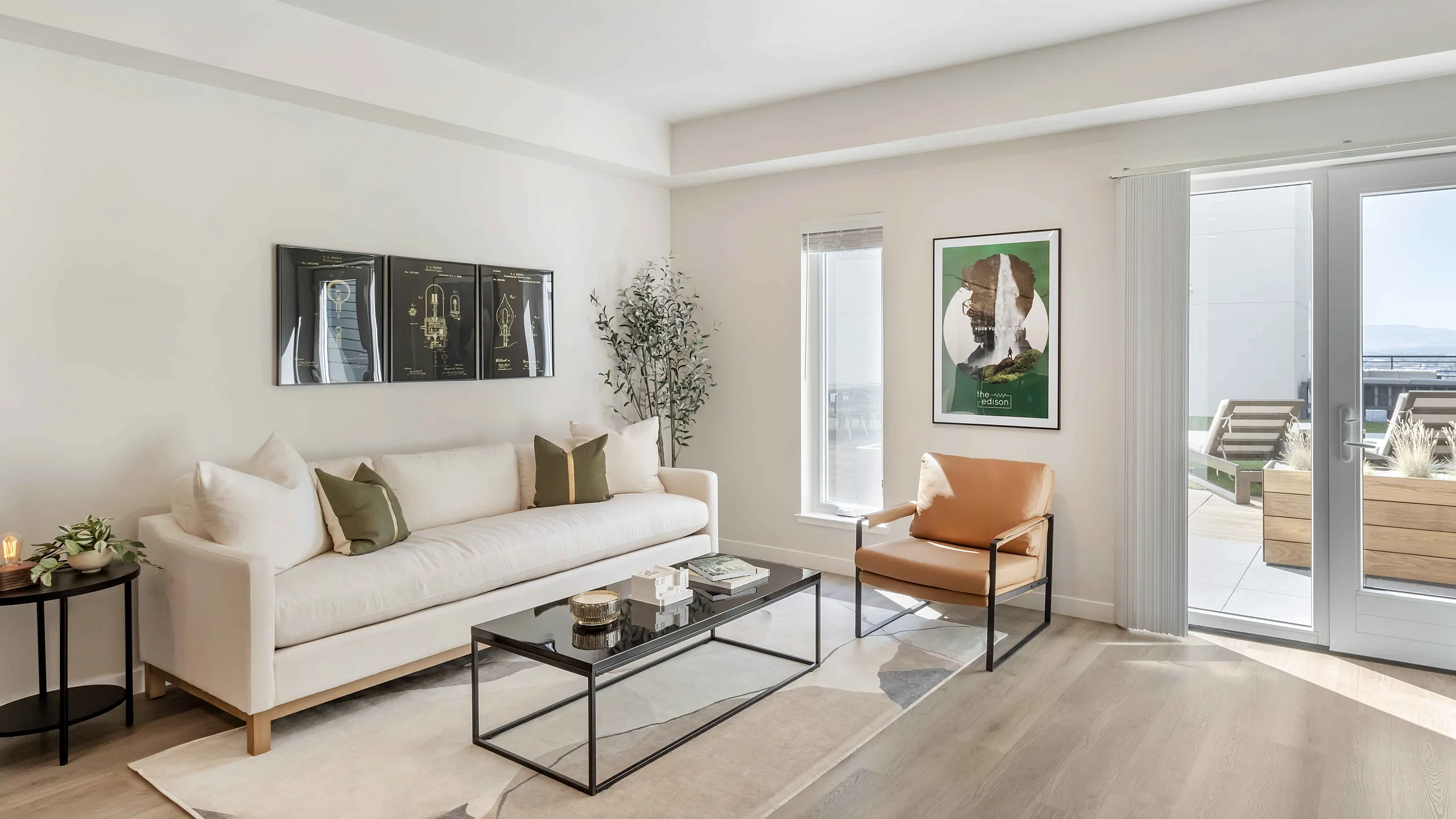 The Edison in Reno, NV bright and modern living room with cozy white sofa, chic artwork, and access to a sunlit balcony with outdoor seating.