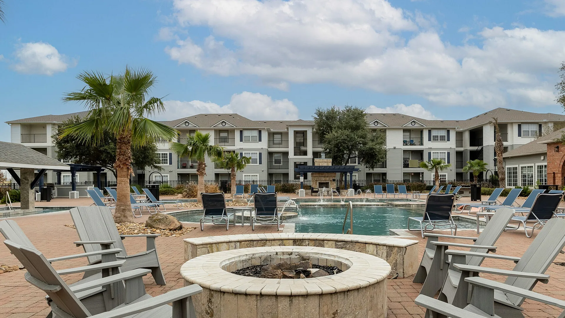 Resort-style pool with palm trees, fire pit, and lounge chairs at The Zone student apartments near TAMU in College Station TX