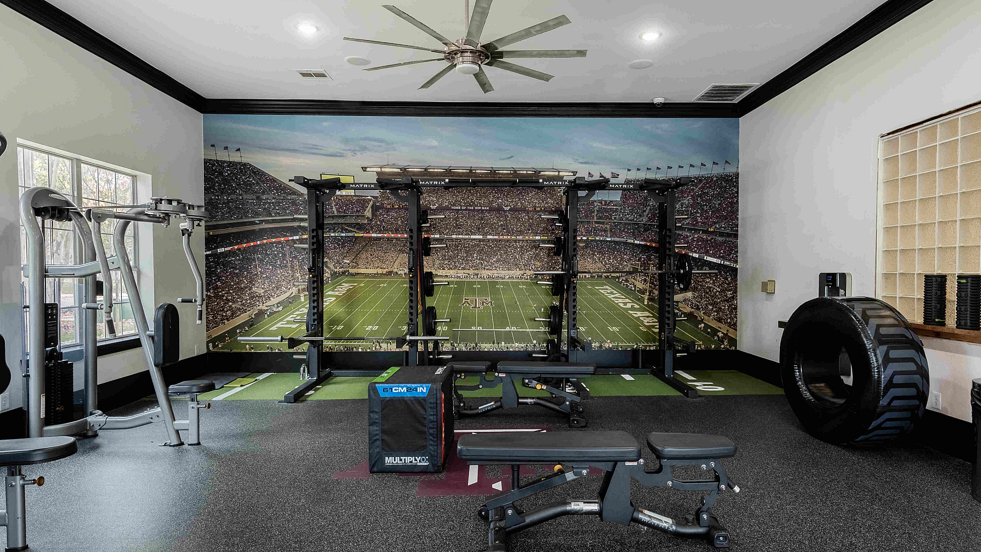 24/7 fitness center with cardio equipment and Aggie mural at The Zone student apartments near TAMU in College Station Texas