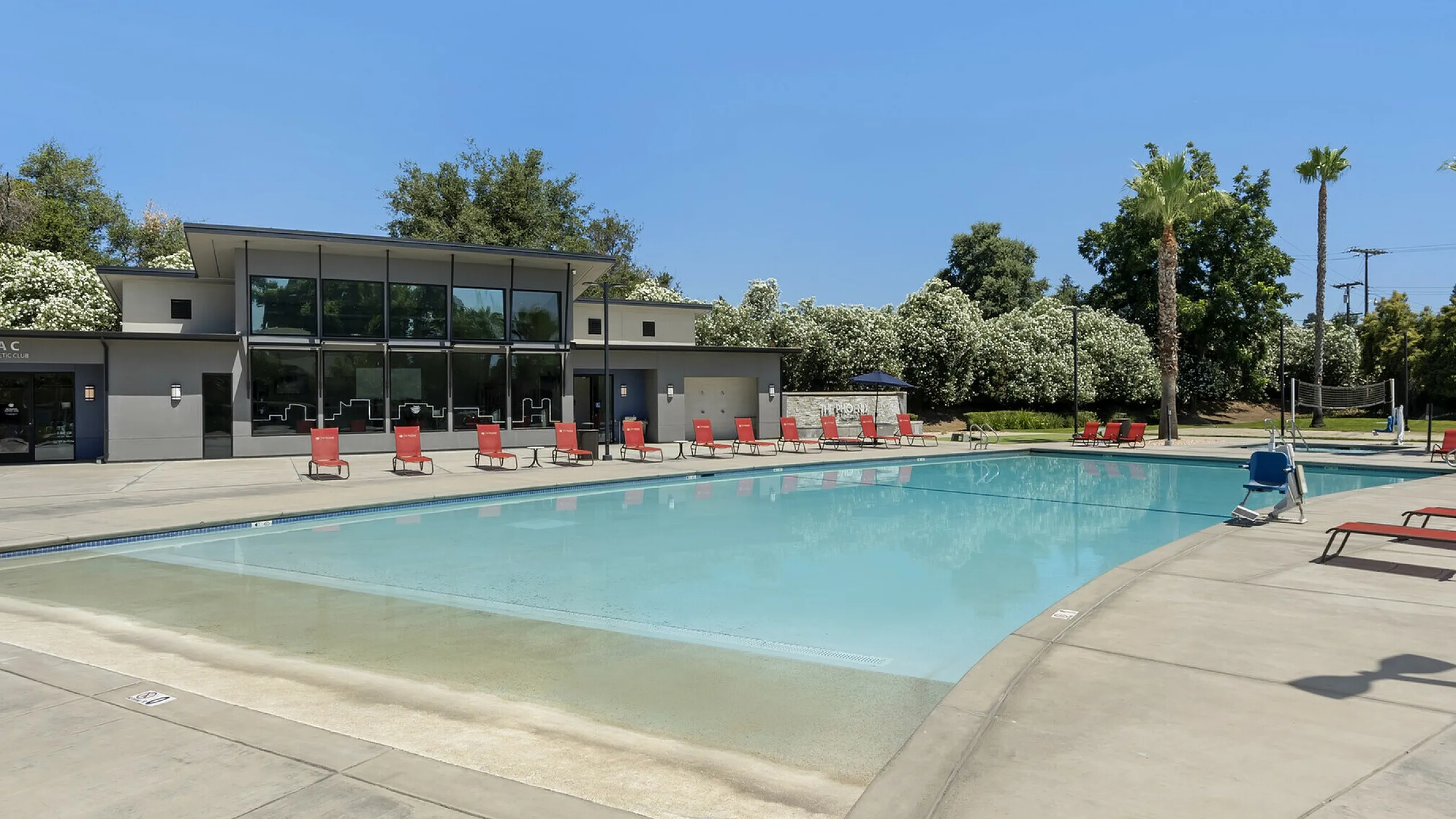 Phoenix Sacramento outdoor pool area with modern amenities, surrounded by lush greenery and stylish red lounge chairs, perfect for relaxation and enjoyment.