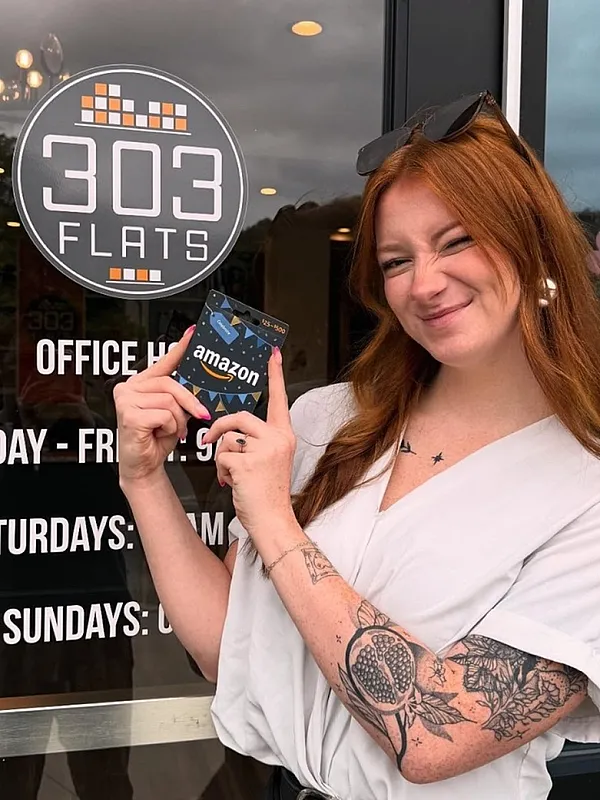 Smiling person holds a gift card in front of '303 Flats' office, highlighting friendly service and welcoming atmosphere.