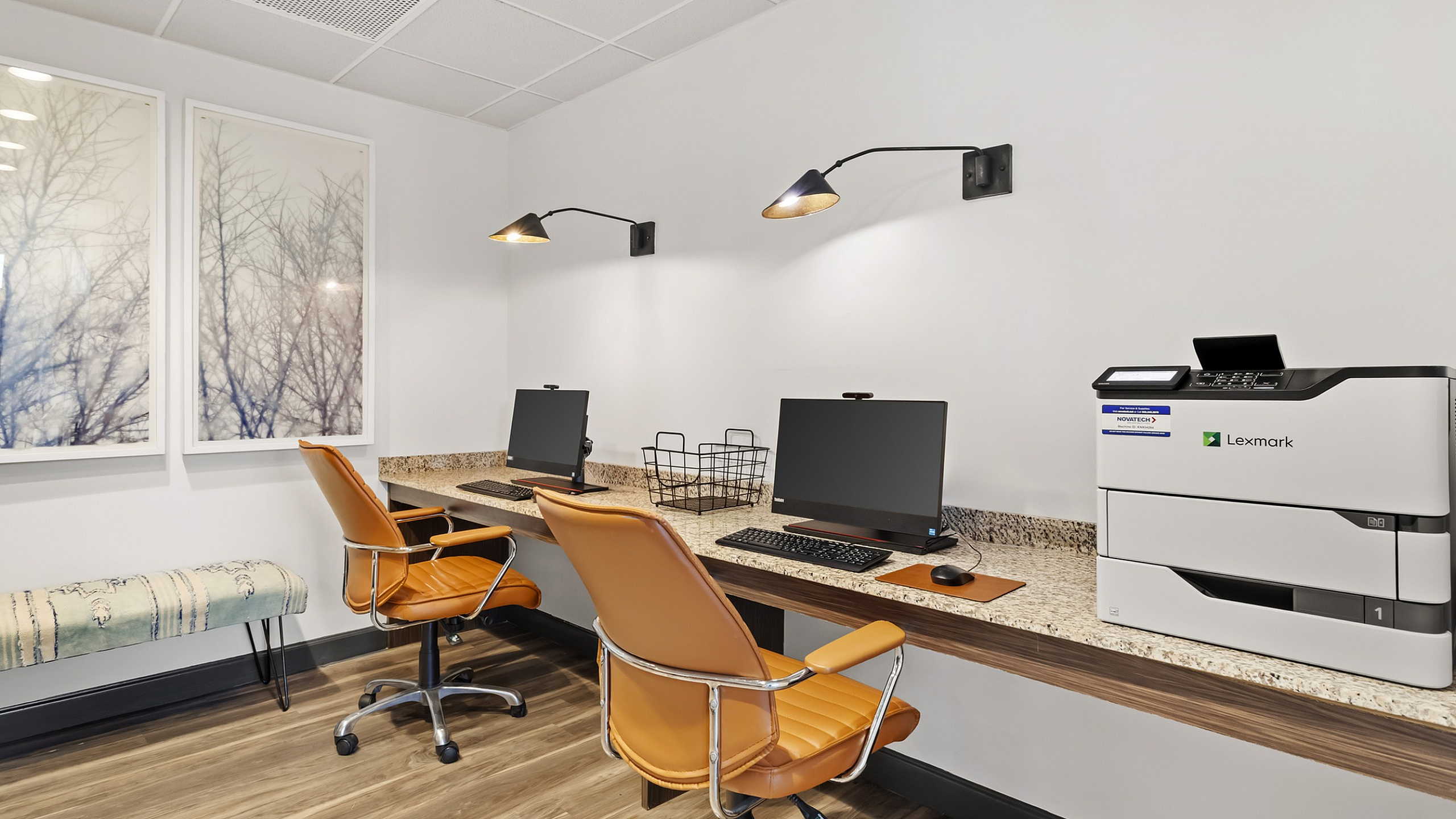 Sophisticated home office in 303 Flats with dual workstations, elegant orange chairs, modern art, and a professional printer on sleek wooden flooring.