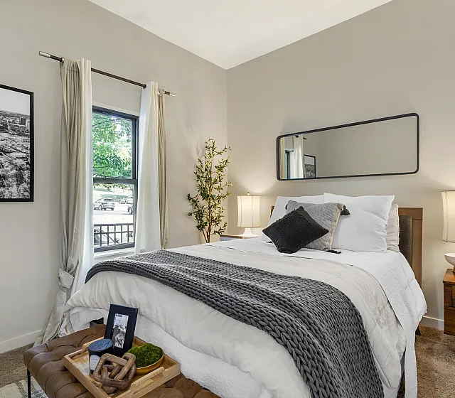Cozy model bedroom with elegant furnishings plush bedding and large window at The Landings apartments Knoxville TN