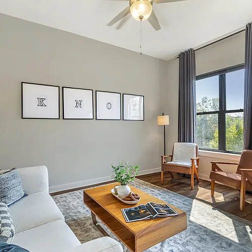 Contemporary model living room with elegant furnishings and large windows overlooking greenery at The Landings apartments Knoxville TN
