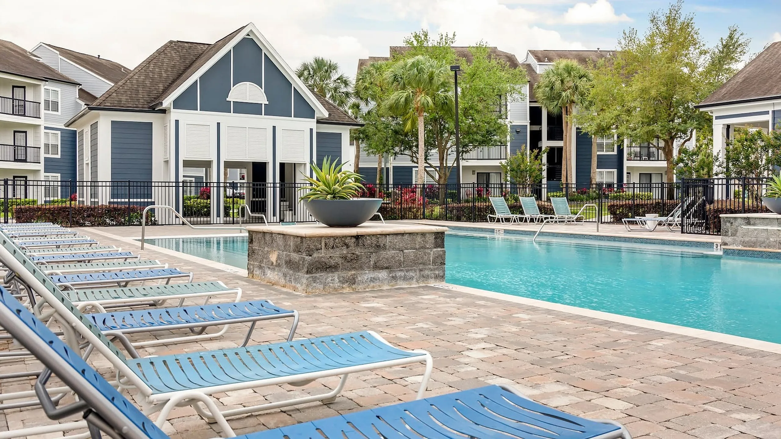 Phoenix Orlando apartment complex with elegant blue buildings and a sparkling outdoor pool, featuring cozy loungers and lush green surroundings.