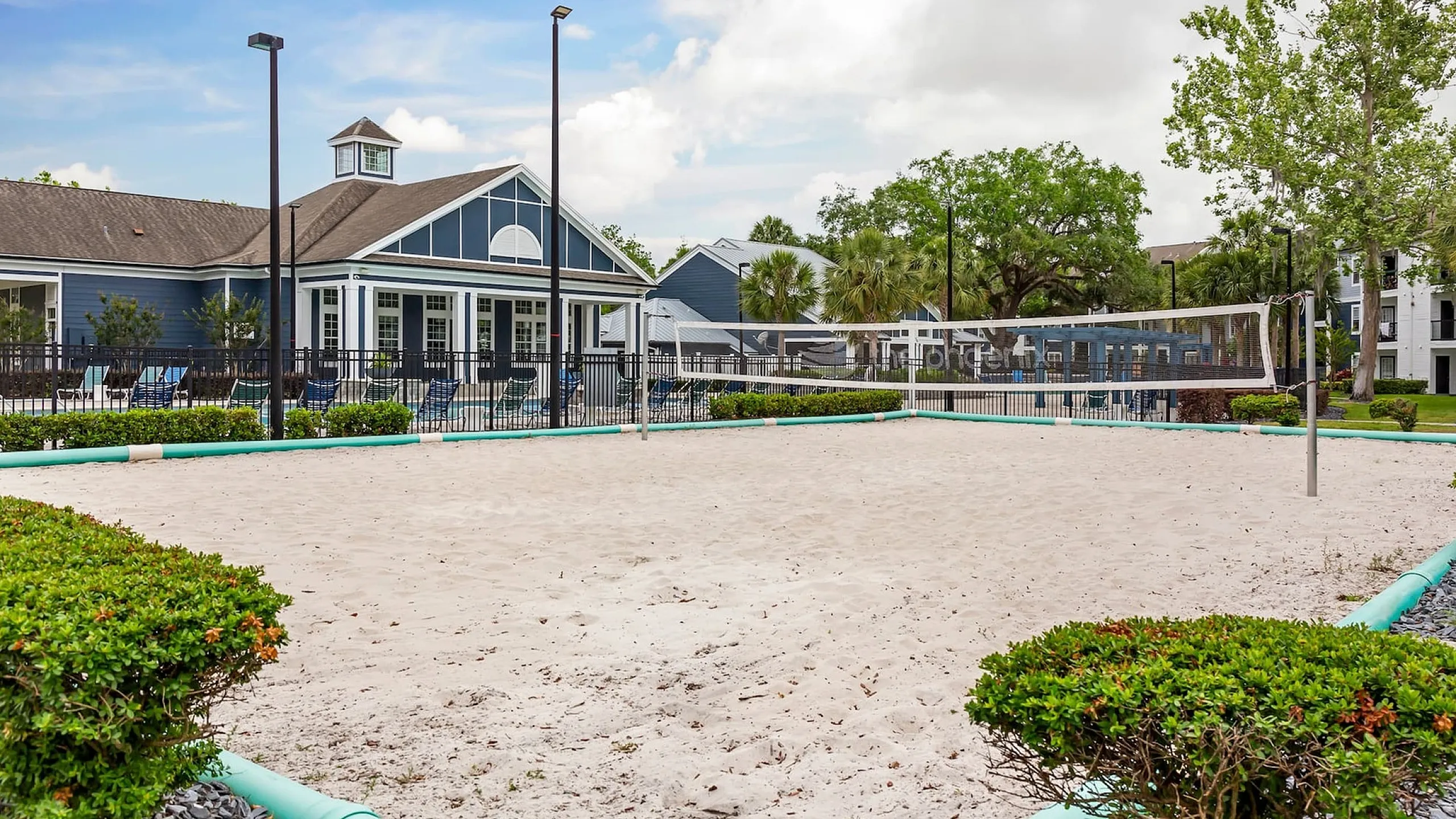 Phoenix Orlando outdoor social area and sand volleyball court surrounded by lush greenery and a modern clubhouse, perfect for recreation and relaxation.