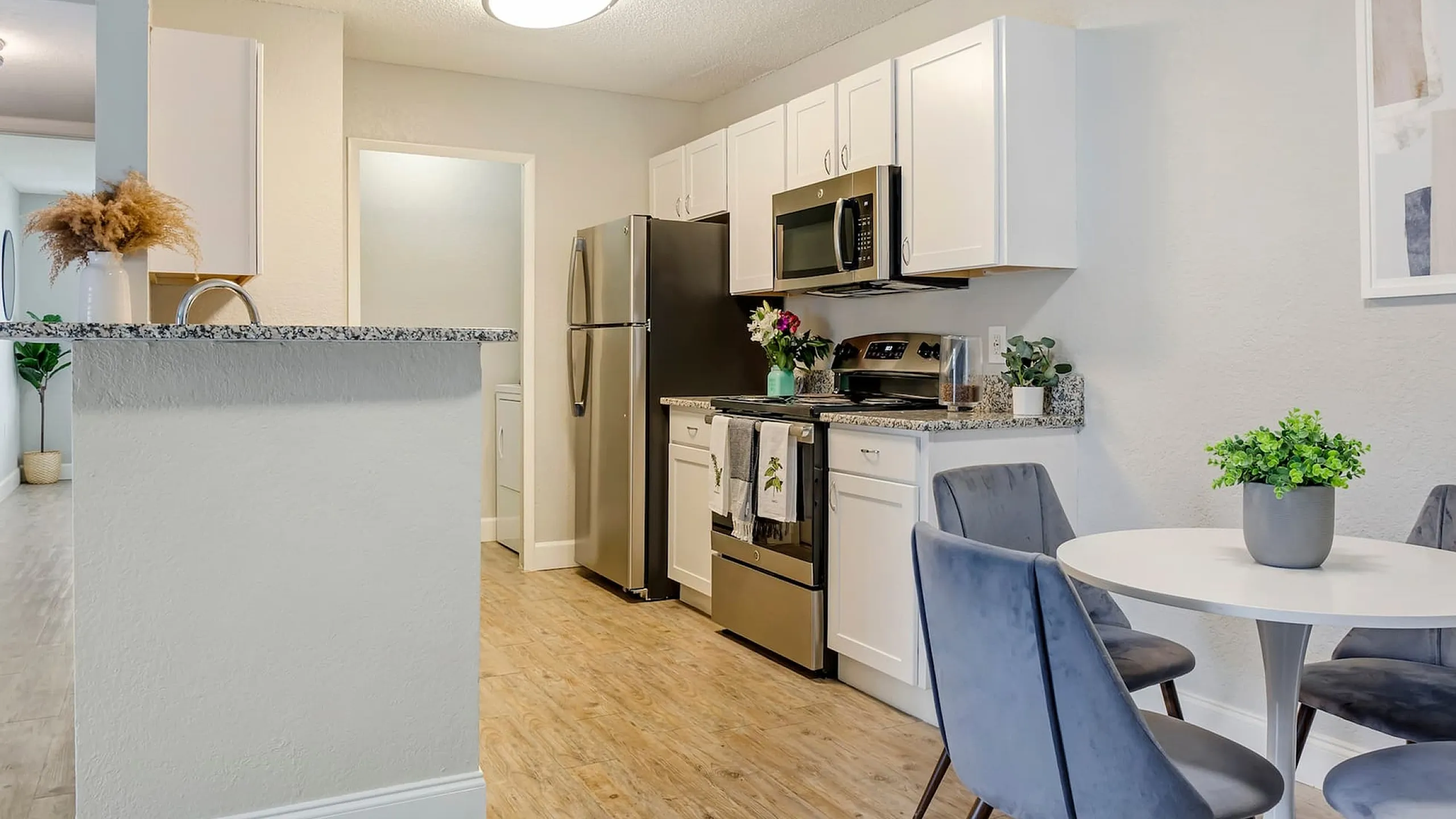 Phoenix Orlando apartment kitchen with granite countertops, white cabinets, and modern stainless steel appliances adjacent to a cozy dining area with plush blue chairs. Ideal for stylish urban living.