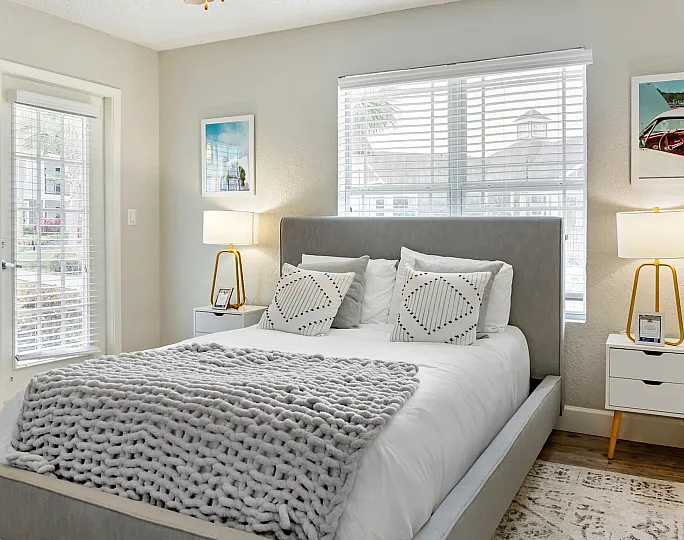 Phoenix Orlando apartment bedroom with modern decor and elegant lighting, featuring a plush bed with stylish cushions and a soft knitted throw.