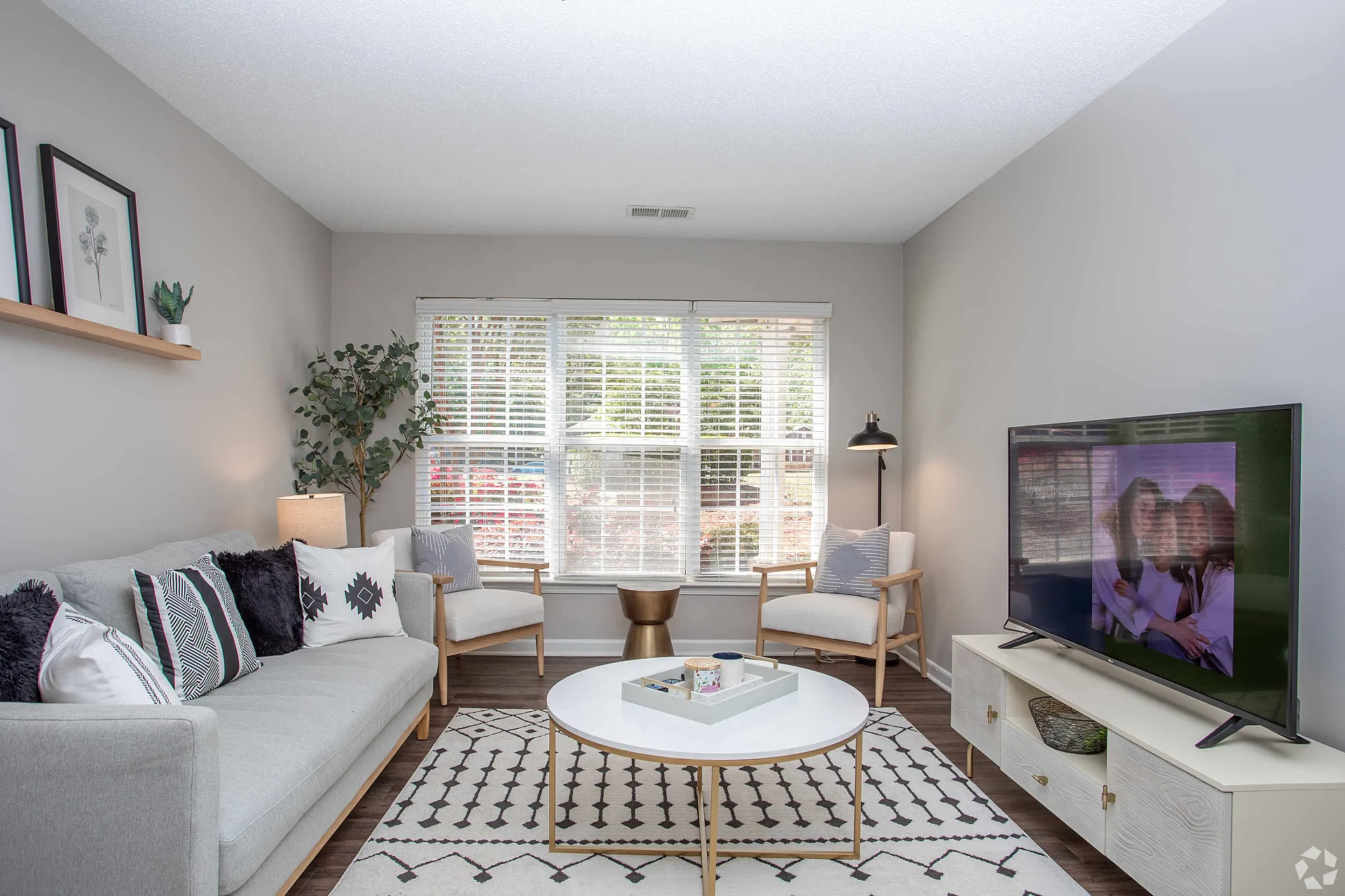 Bright and inviting living room with modern decor, featuring a comfortable grey sofa, stylish white chairs, large window with natural light, and a sleek TV setup.