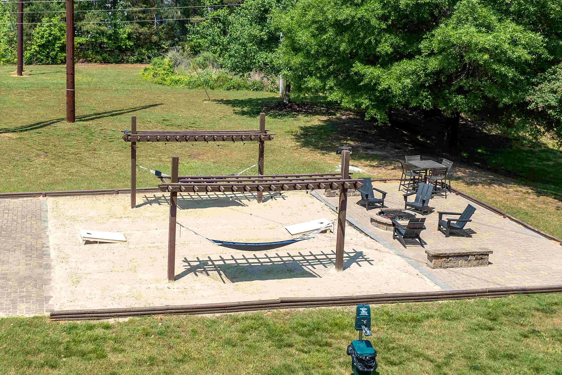 Inviting outdoor patio area with lush greenery, featuring a cozy hammock under wooden pergolas, relaxing lounge chairs, and dining space, perfect for social gatherings.