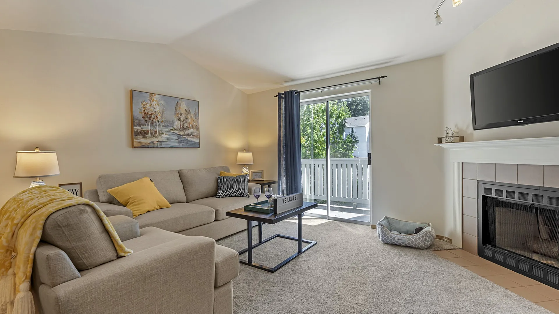 Inviting living room with comfortable seating, modern decor, and a cozy fireplace, featuring large windows opening to a sunny balcony.