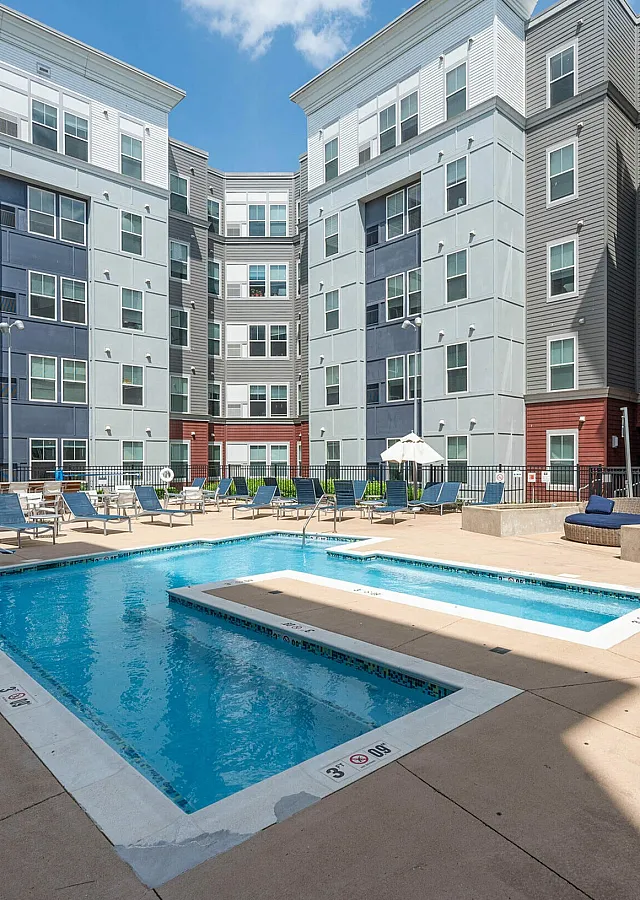 Modern apartment complex featuring a vibrant outdoor pool area with lounge chairs and umbrellas, perfect for relaxation and leisure.