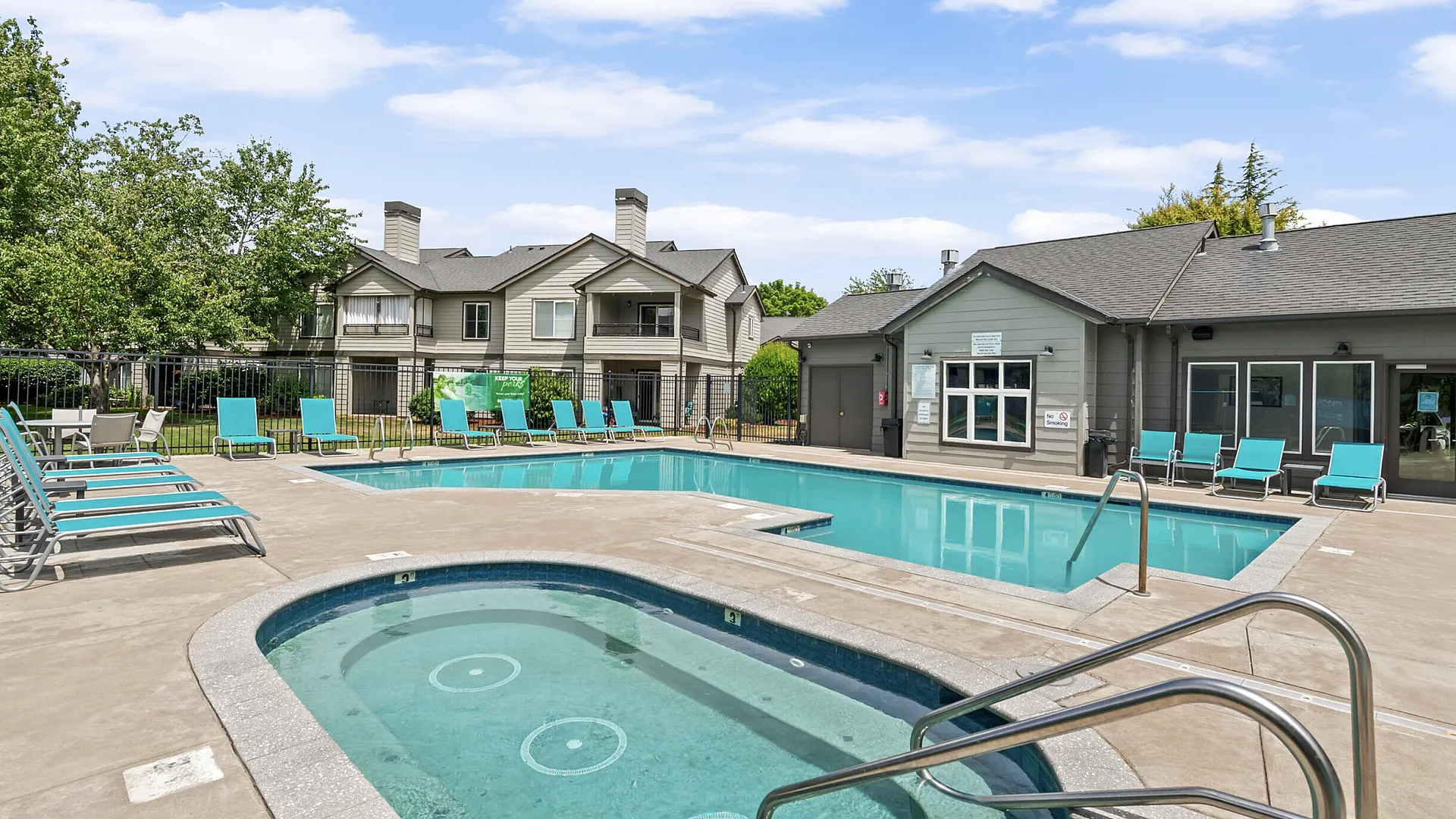 Inviting outdoor pool area with modern lounge chairs, spa, and charming apartment backdrop under a bright blue sky.