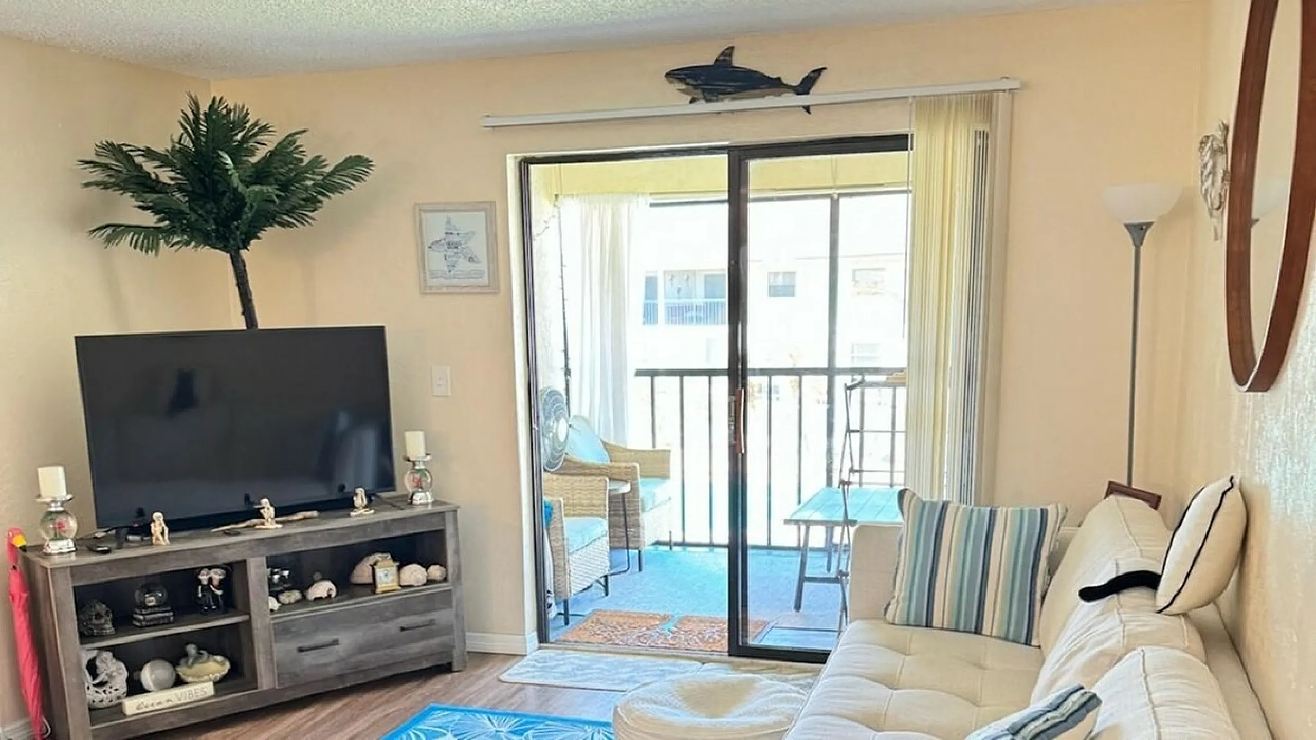 Cozy living room with a welcoming ambiance featuring a plush sofa, modern TV setup, and charming decor accents, leading to a bright balcony area through sliding glass doors.