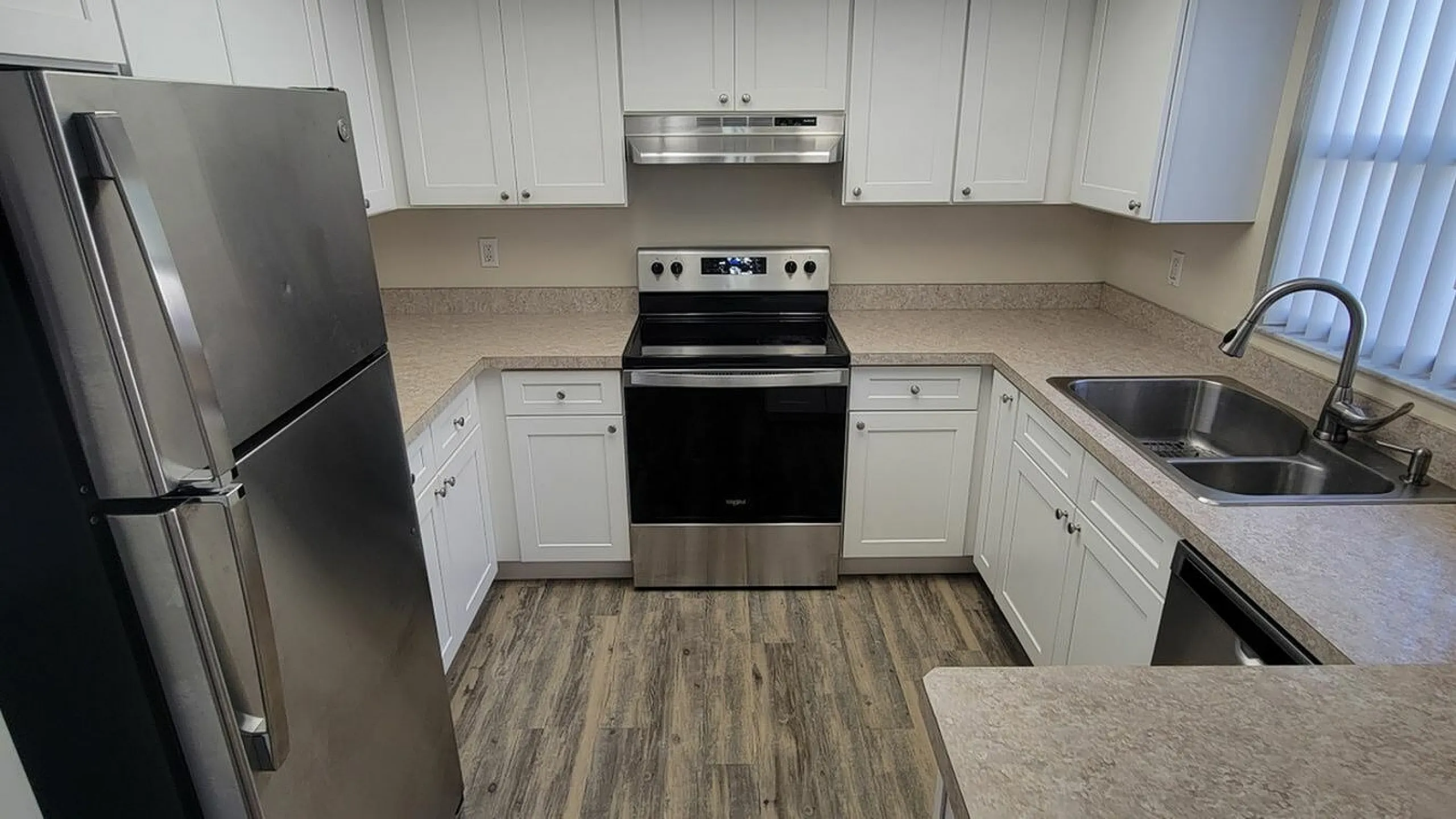 Modern kitchen with sleek stainless steel appliances, elegant white cabinetry, and stylish wood flooring.