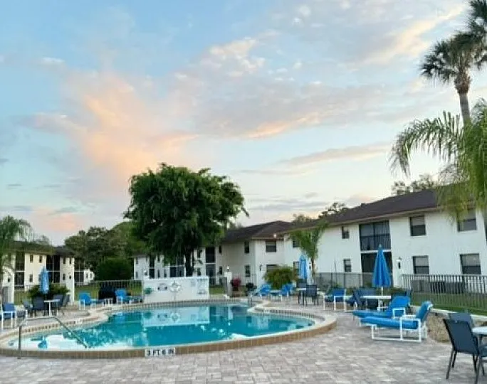 Beautiful apartment complex with a sparkling pool, surrounded by lush greenery and cozy outdoor seating, perfect for relaxation and leisure.