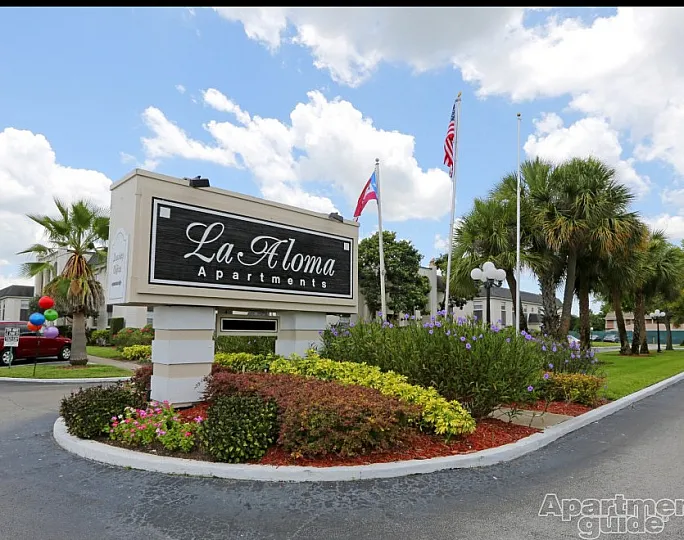 Charming La Aloma Apartments entrance surrounded by lush greenery and vibrant flags, offering a welcoming and serene community living experience.