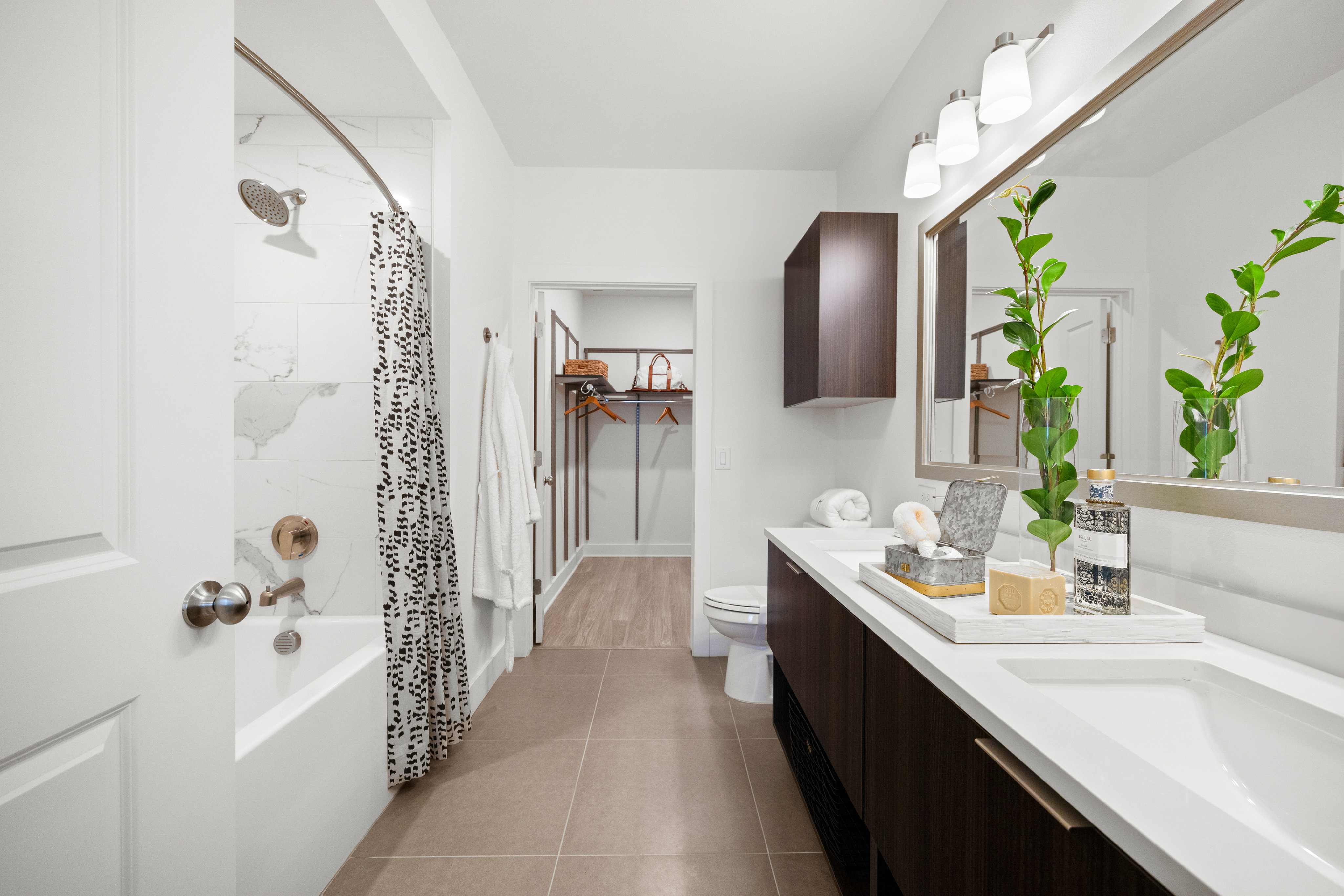 apartment bathroom with double vanity and soaking tub leading to walk-in closet.