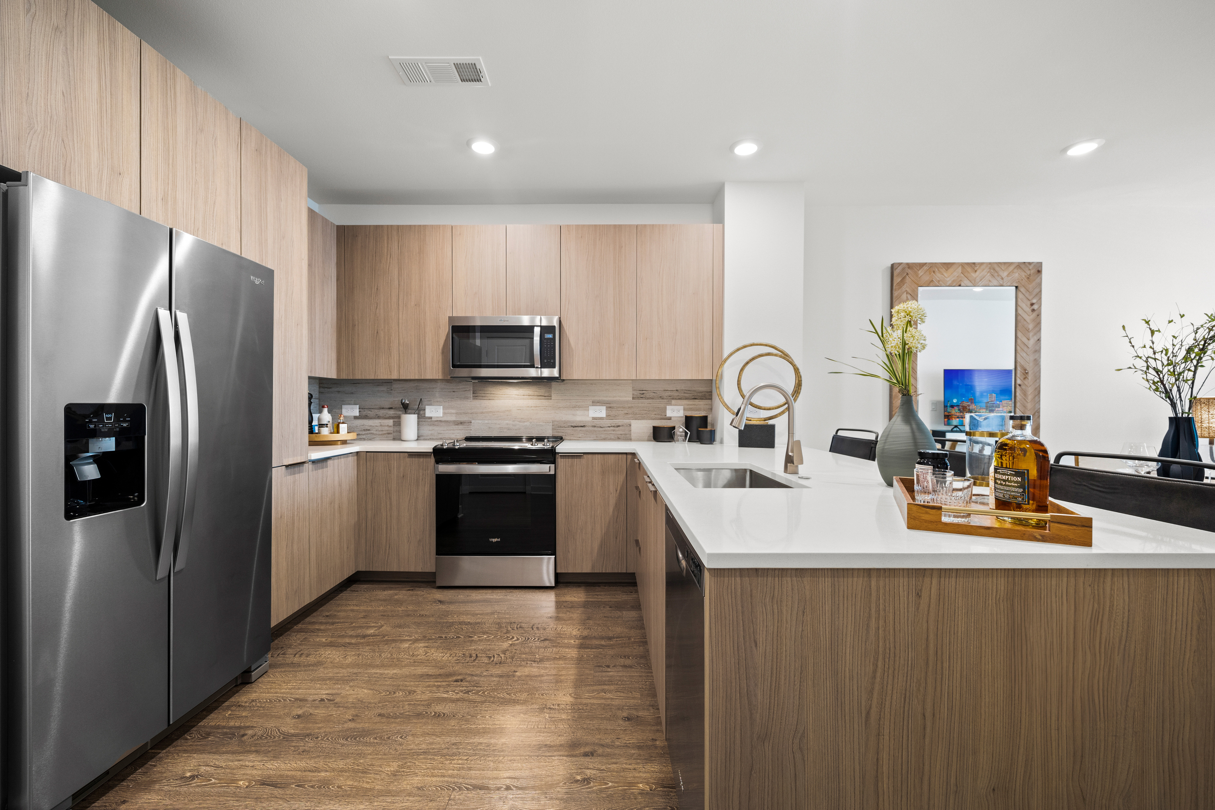 U-shaped apartment kitchen with stainless steel appliances, wood-style cabinetry, and white quartz countertops