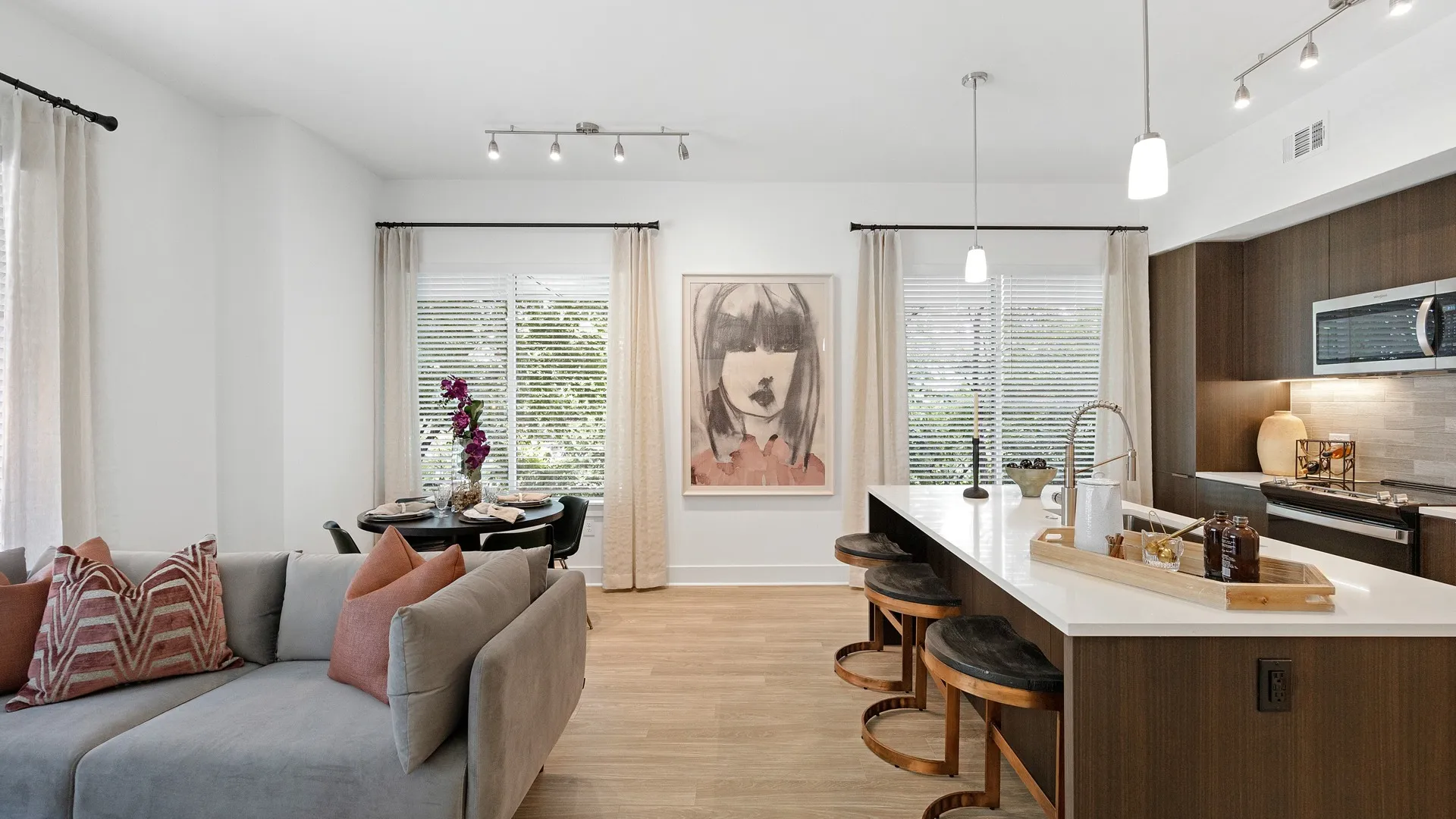 Kitchen with dark wood cabinetry and white counters, counter-height seating and kitchen island with sink, adjacent to living room sofa and round dining table