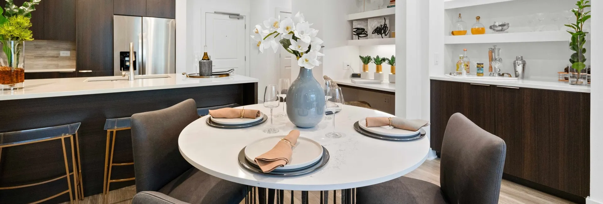 dining area with round white table built-in dry bar, desk, and kitchen with dark cabinets and stainless steel fridge