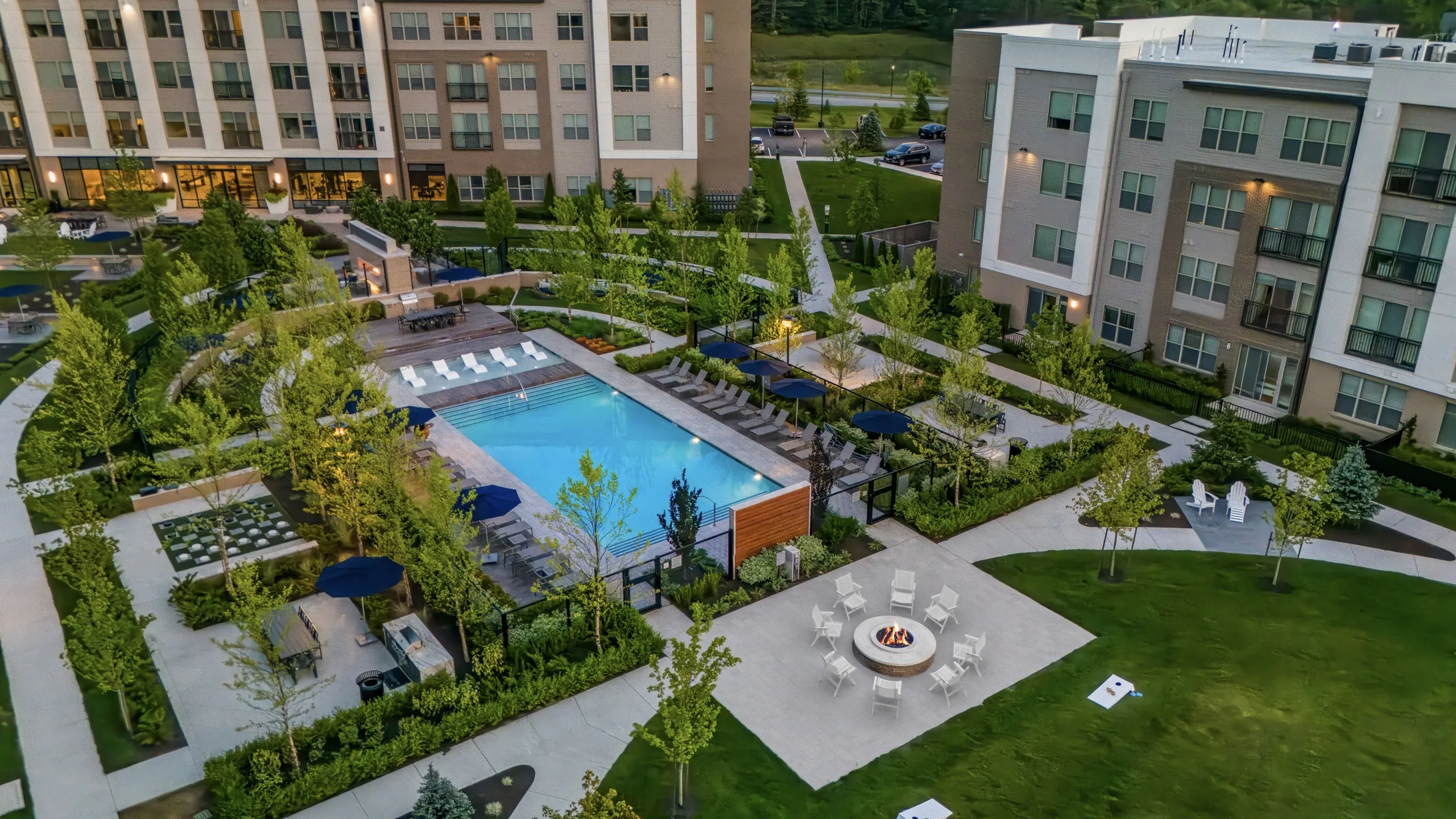 apartment community with multiple 4-story buildings around resort-style pool and expansive courtyard with outdoor games, lounge seating and fireplaces