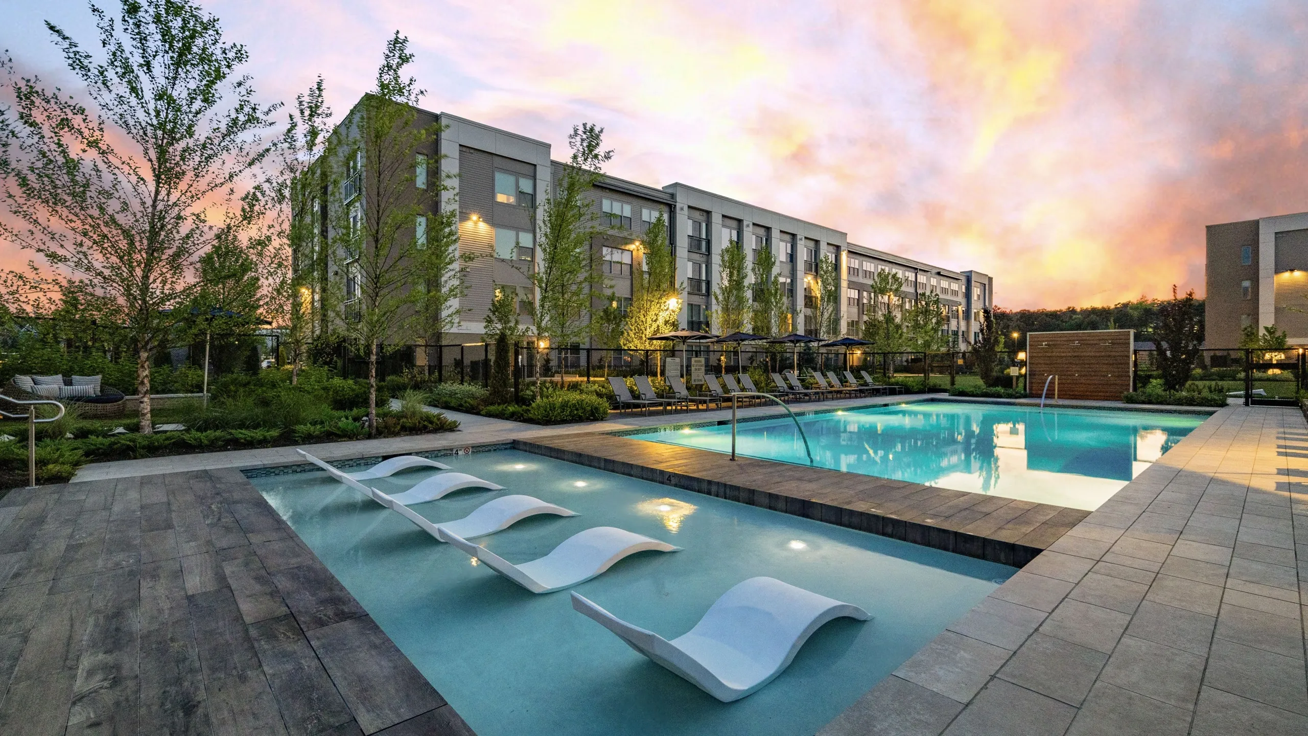 4-story apartment building with resort style pool at sunset with lounge chairs and umbrellas and outdoor showers