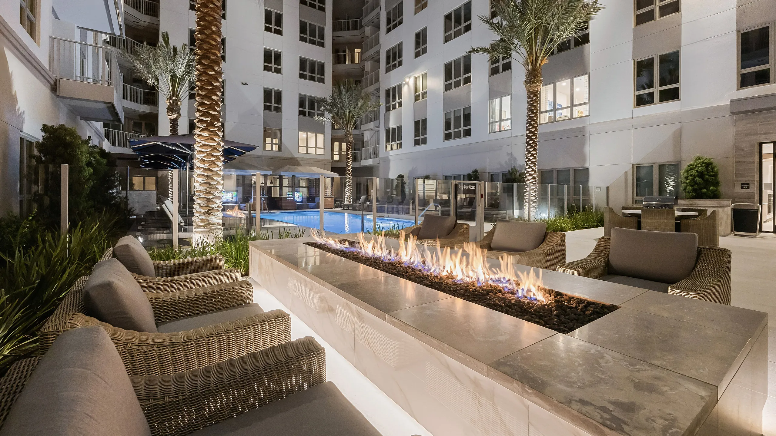 courtyard of 6-story apartment building with rectangular open fire pit surrounded by 6 cushioned chairs