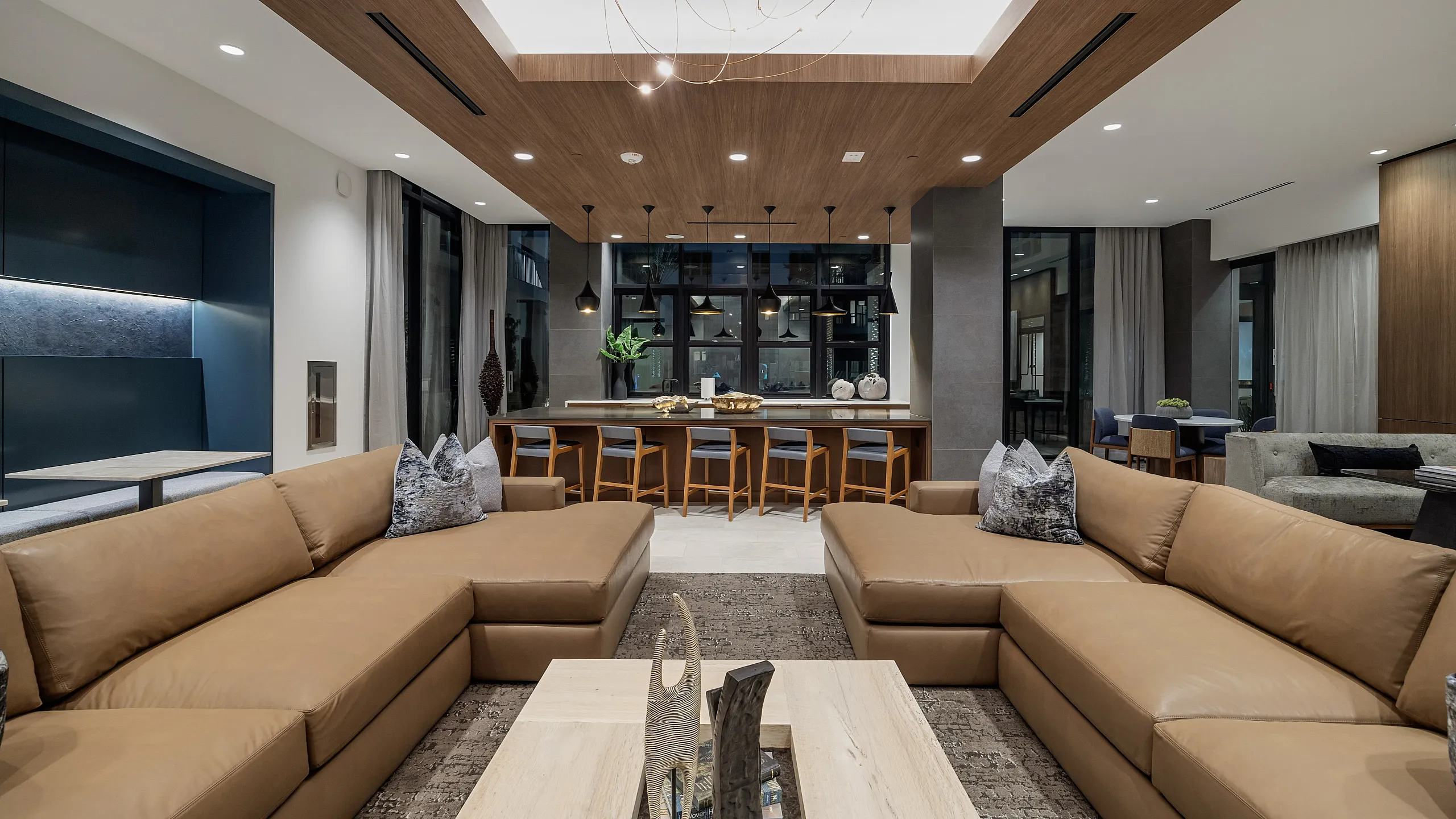 amenity club room in apartment with two sectional sofas in front of kitchen area with counter seats and pendant lighting