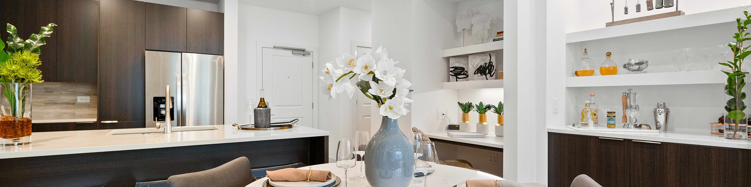 apartment dining area with a round table set for four, adjacent to a kitchen with dark wood cabinetry and stainless steel appliances.