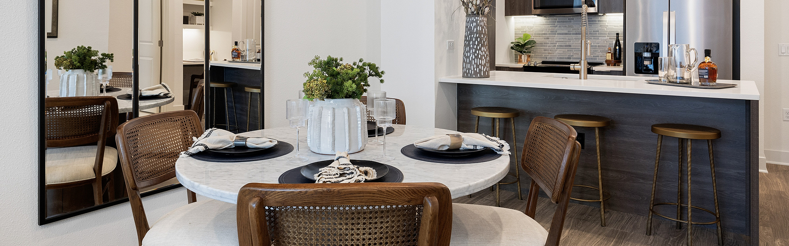 apartment dining area with round dining table, wooden chairs, and a kitchen with stainless steel appliances.