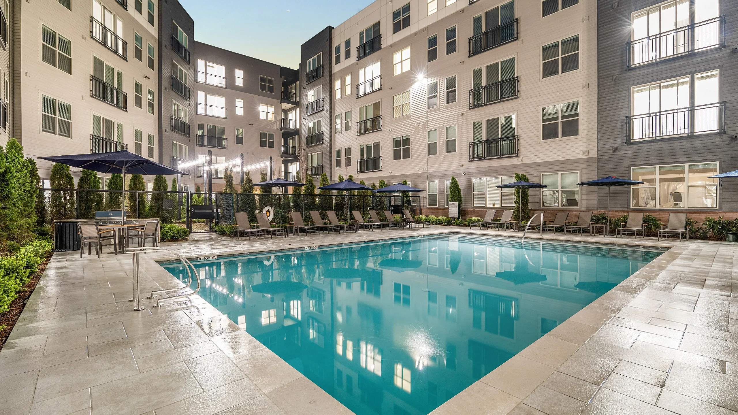 Luxurious apartment complex with a sparkling outdoor swimming pool, lined with cozy lounge chairs and surrounded by modern architecture.