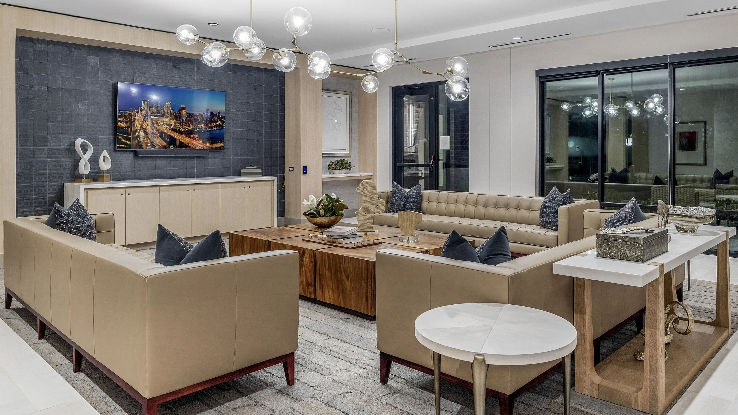 Elegant living room with modern decor, featuring plush beige sofas, stylish chandelier, and large flat-screen TV on a dark accent wall. Perfect for sophisticated gatherings.