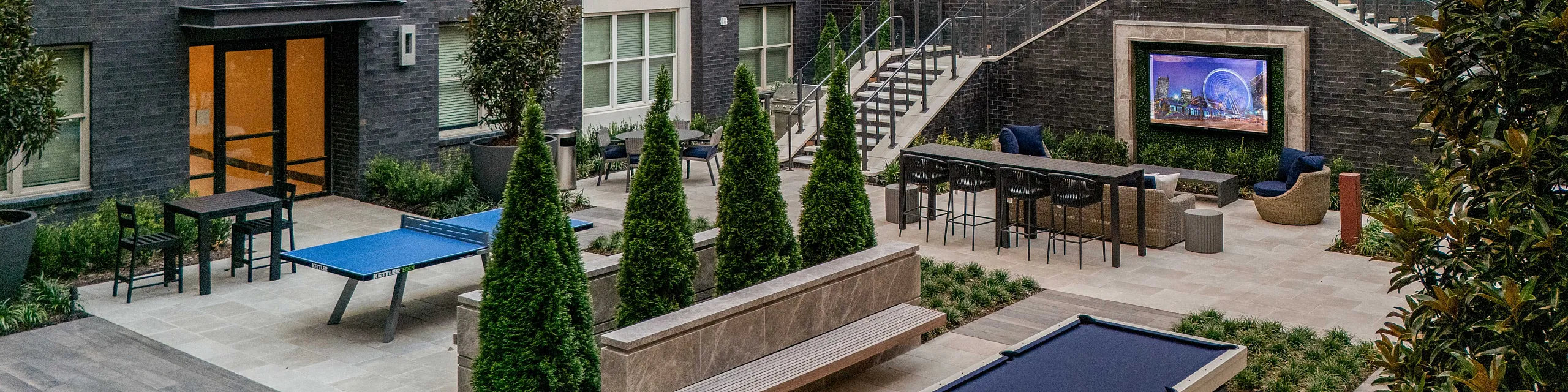 Elegant urban courtyard with lush landscaping, a ping pong table, and outdoor seating area, perfect for leisure and social gatherings.