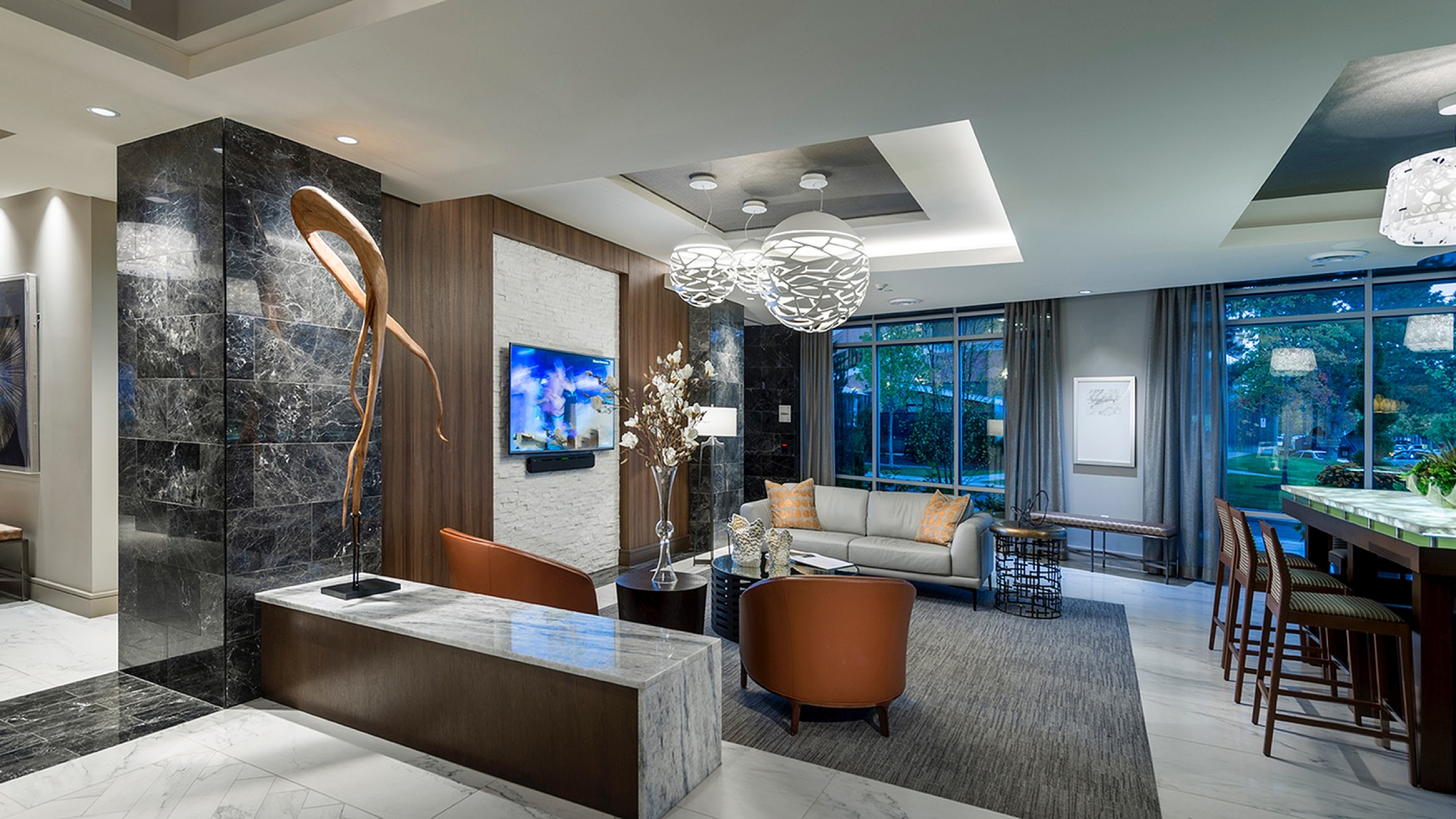 Luxurious and modern living room with elegant decor, marble accents, and a stylish open-concept bar, illuminated by creative chandeliers.