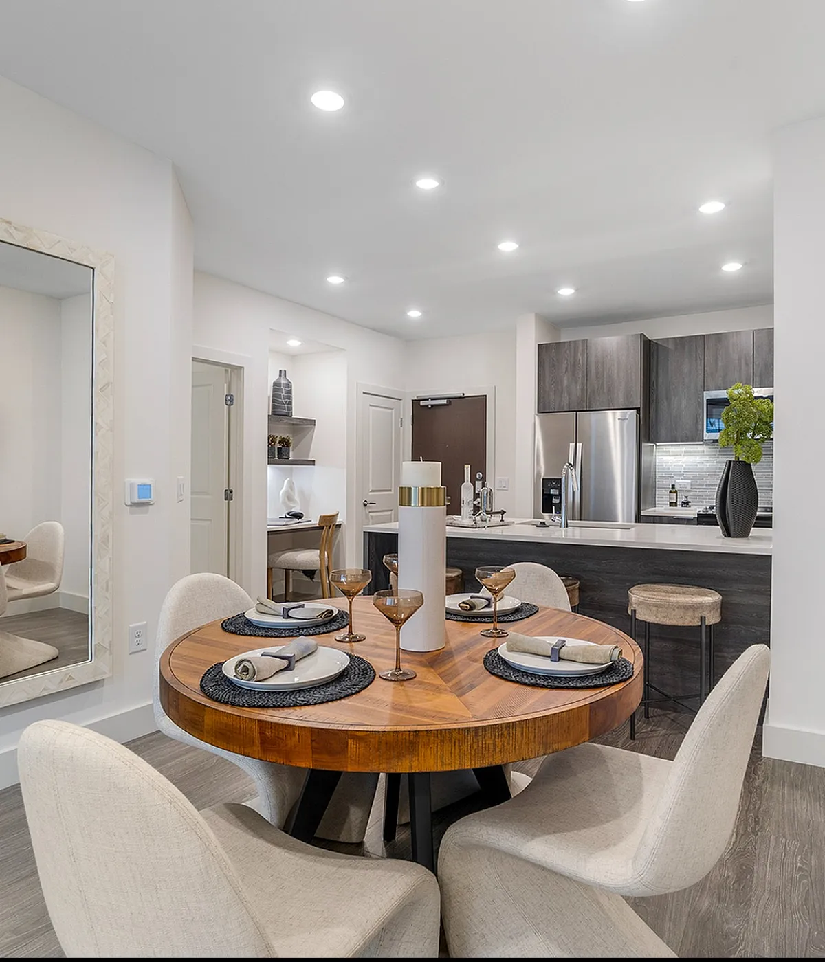 Modern open-concept dining area featuring a chic round wooden table set for four, adjacent to a stylish kitchen with sleek cabinets and stainless steel appliances.