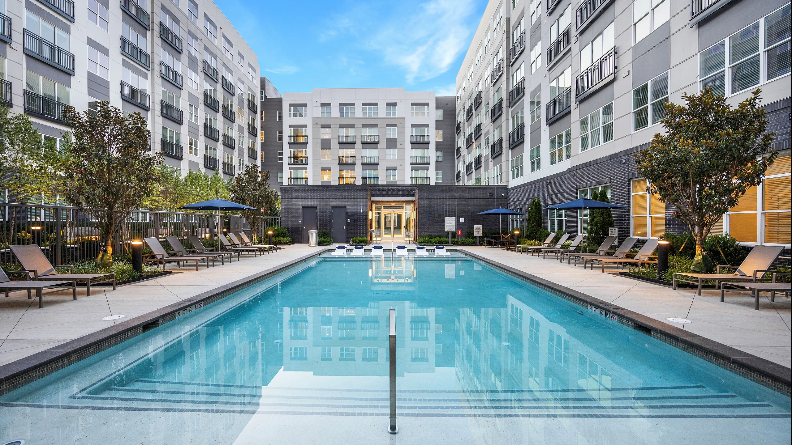 Luxurious apartment complex featuring a sparkling outdoor pool surrounded by comfortable lounge chairs and lush greenery, perfect for relaxation and leisure.