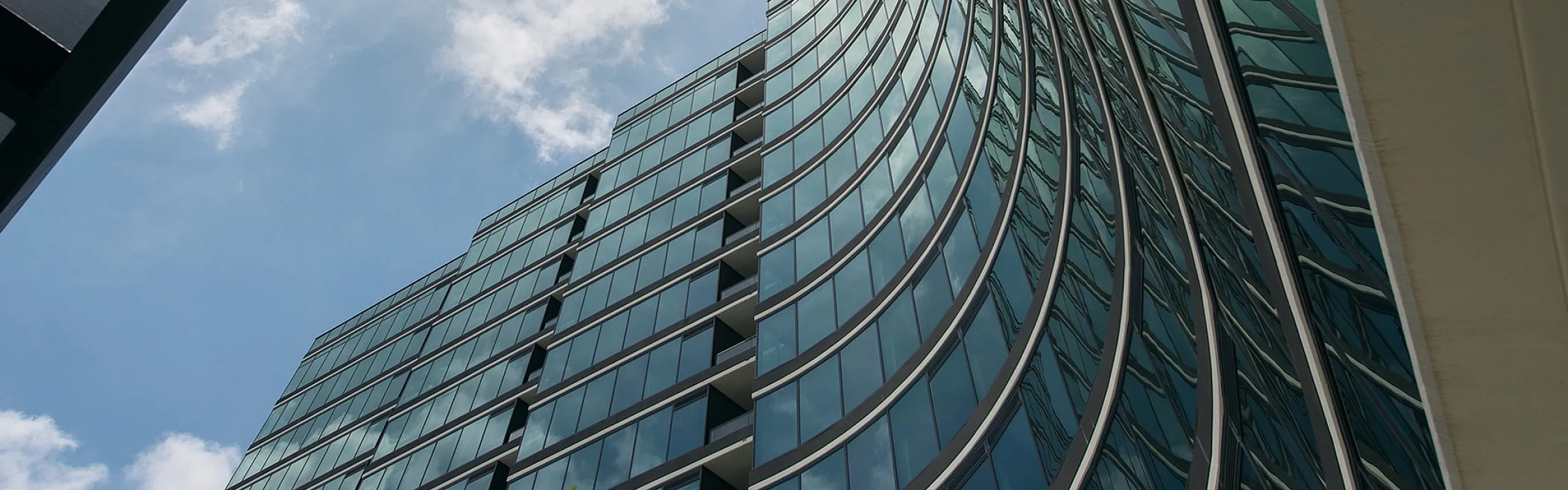 Striking modern architecture with sleek curved glass facade and sunlit sky reflection.