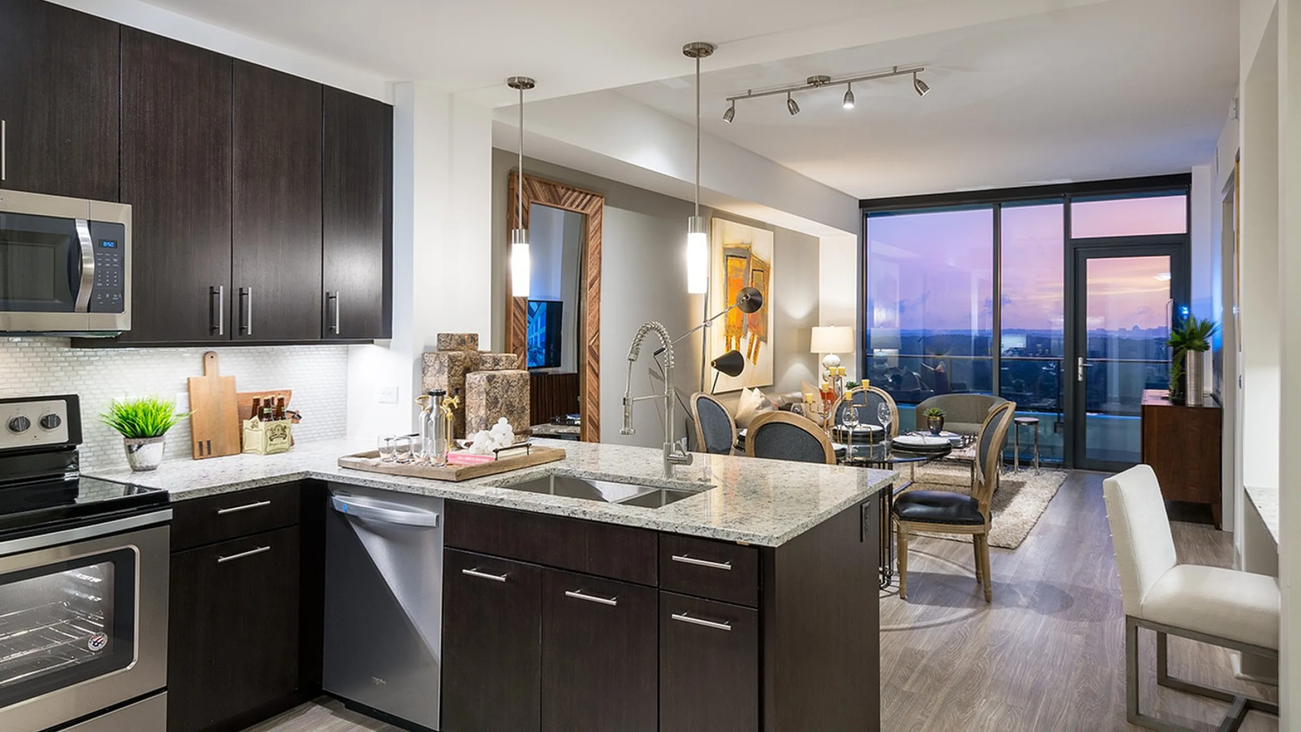 Contemporary open-plan kitchen and living area in luxury apartment with sleek design, warm lighting, and stunning sunset view through floor-to-ceiling windows.