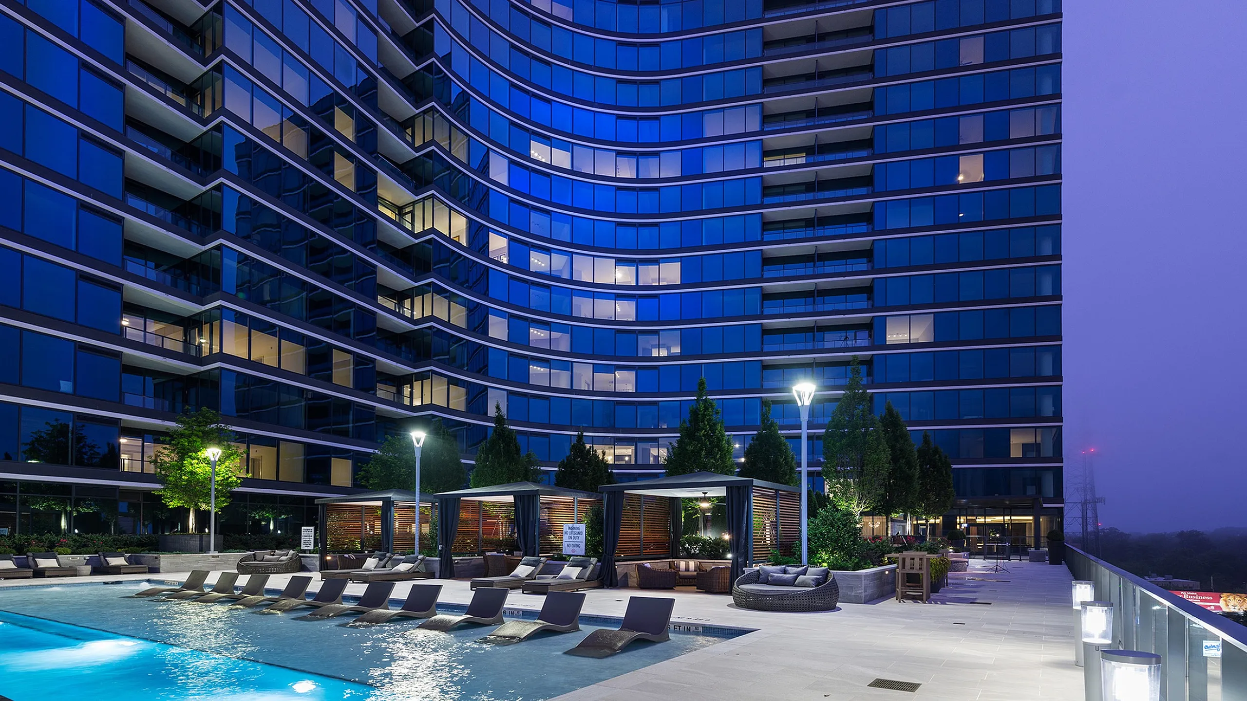 Stunning modern apartment building with sleek glass facade and elegant outdoor pool area at dusk.