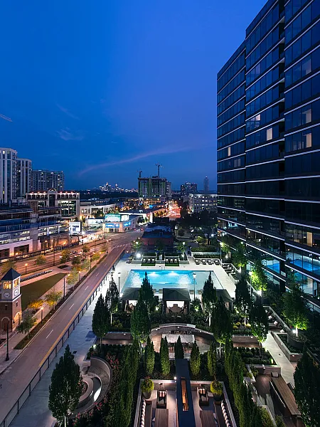 Stunning cityscape at dusk with luxurious high-rise apartments, illuminated pool, and lush landscaped gardens offering an upscale urban living experience.